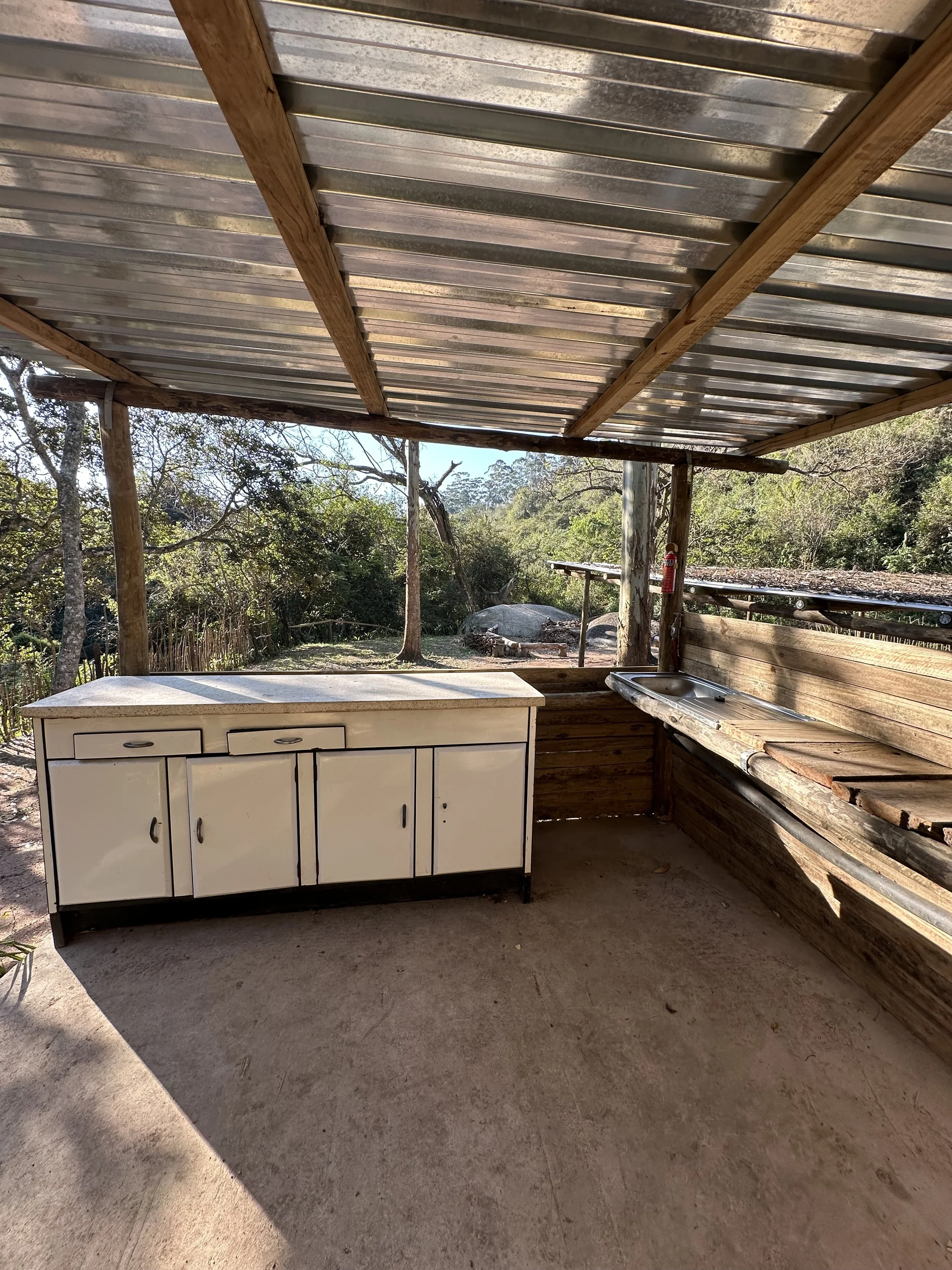 Outdoor sink with wooden structure surrounded by greenery in a natural setting.