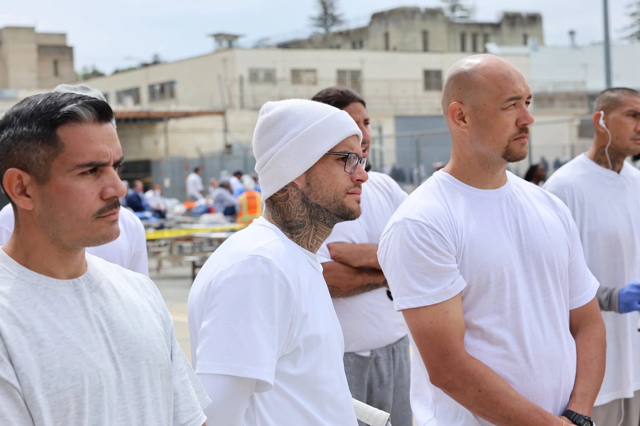 People wearing white shirts standing outdoors at a community service event with tables and volunteers in the background.