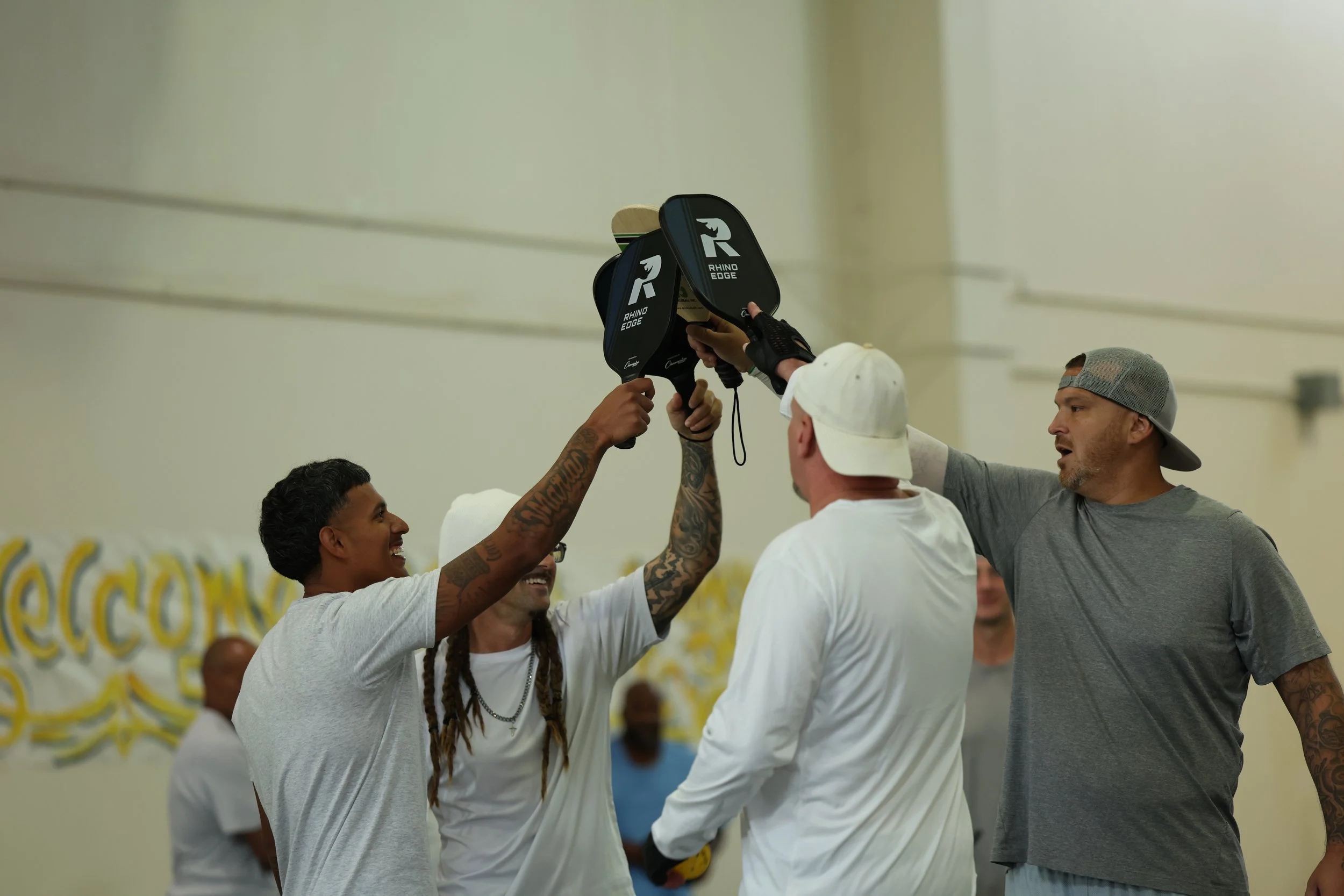 Four male prison inmates smiling during a pickleball game.