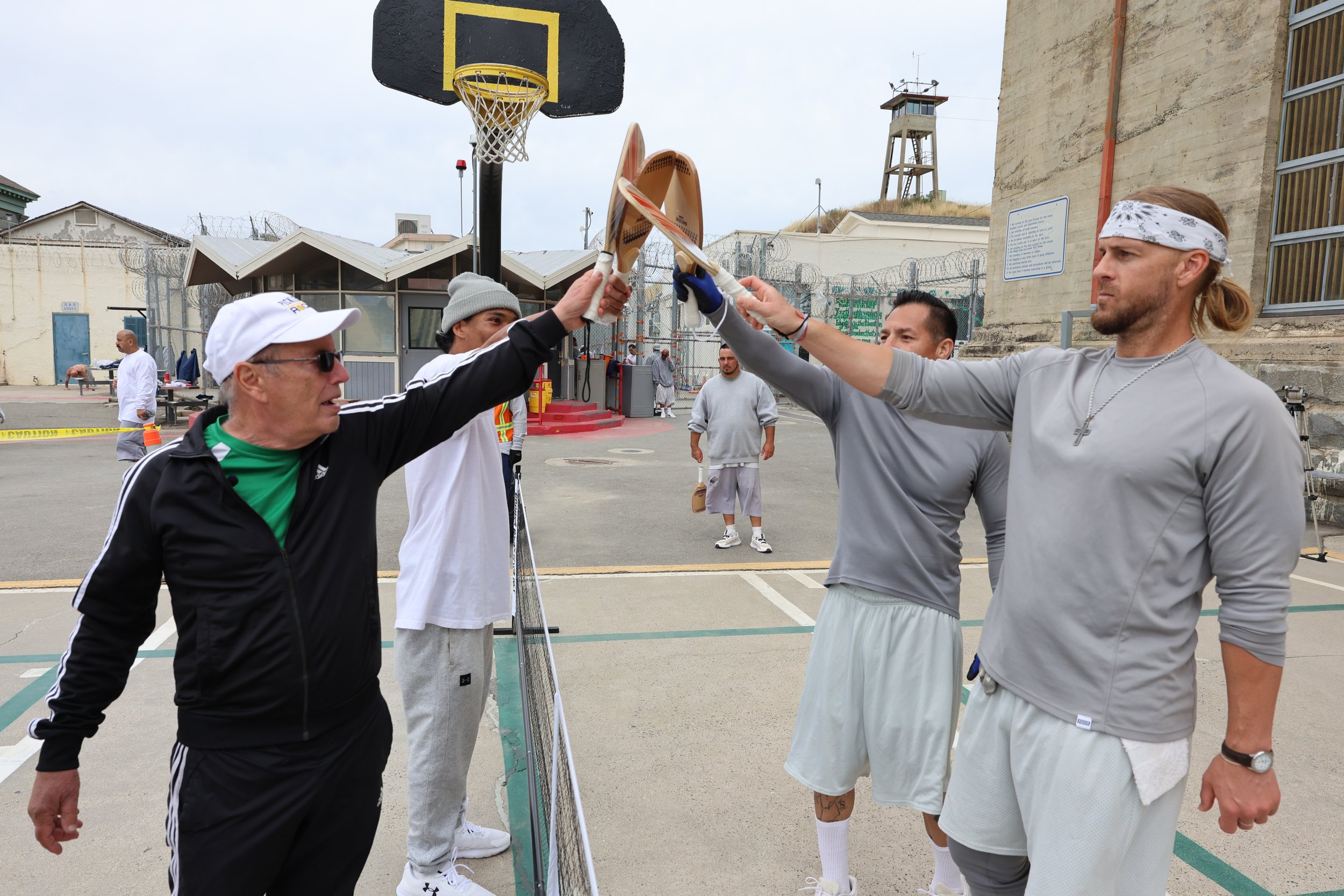 Four male prison inmates smiling during a pickleball game.