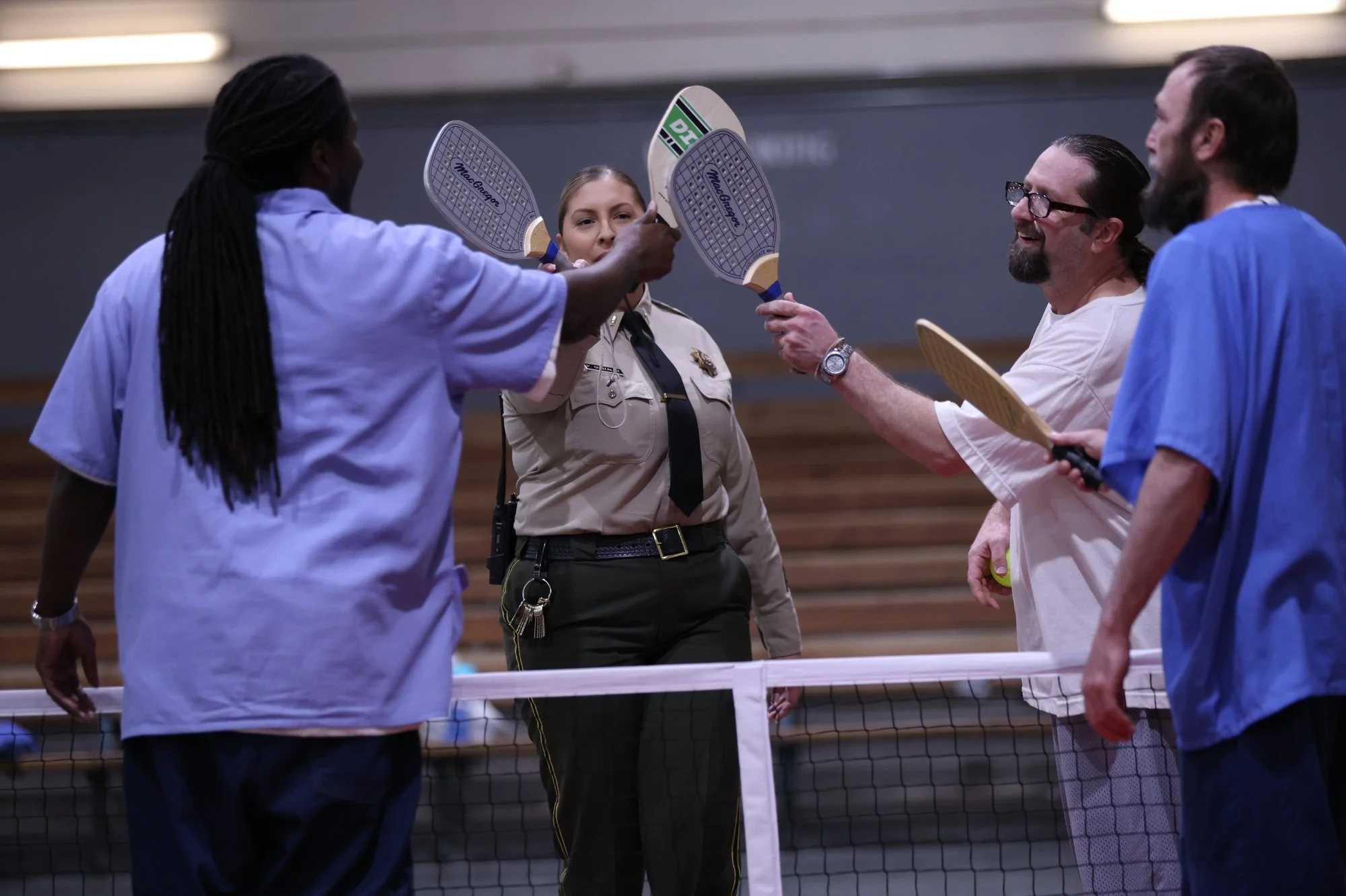People playing pickleball on an indoor court, with some holding paddles and a woman in a police uniform.