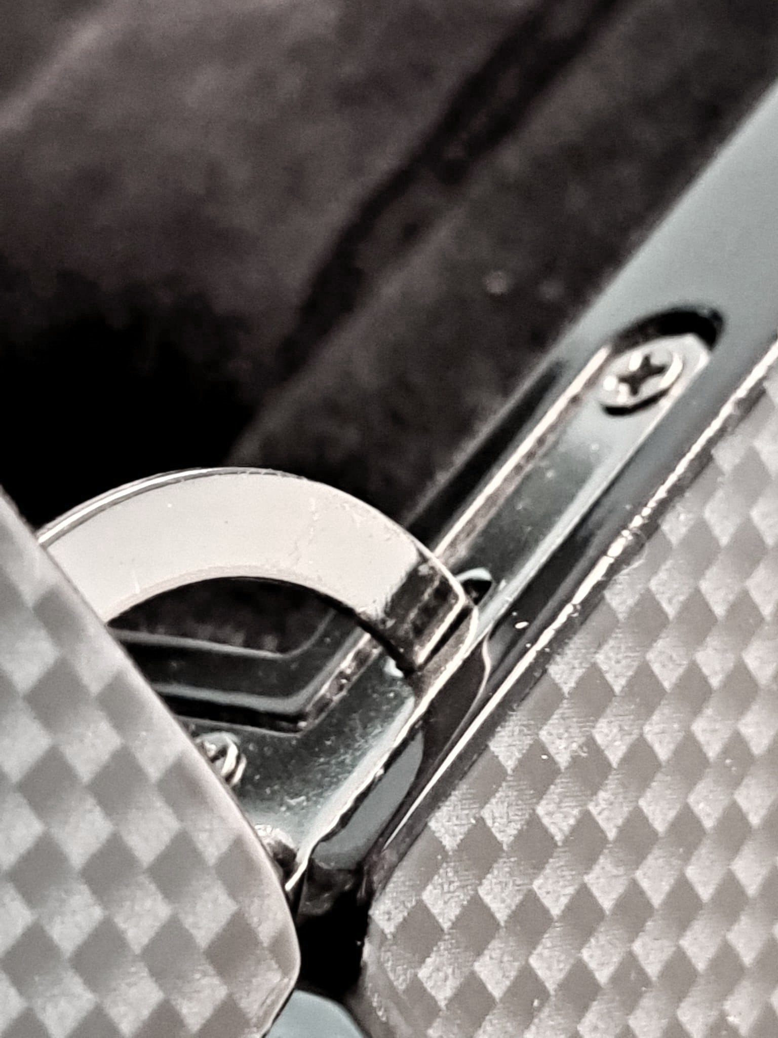 Dettaglio di una chiusura metallica di una valigia con motivo a scacchi grigi e neri.