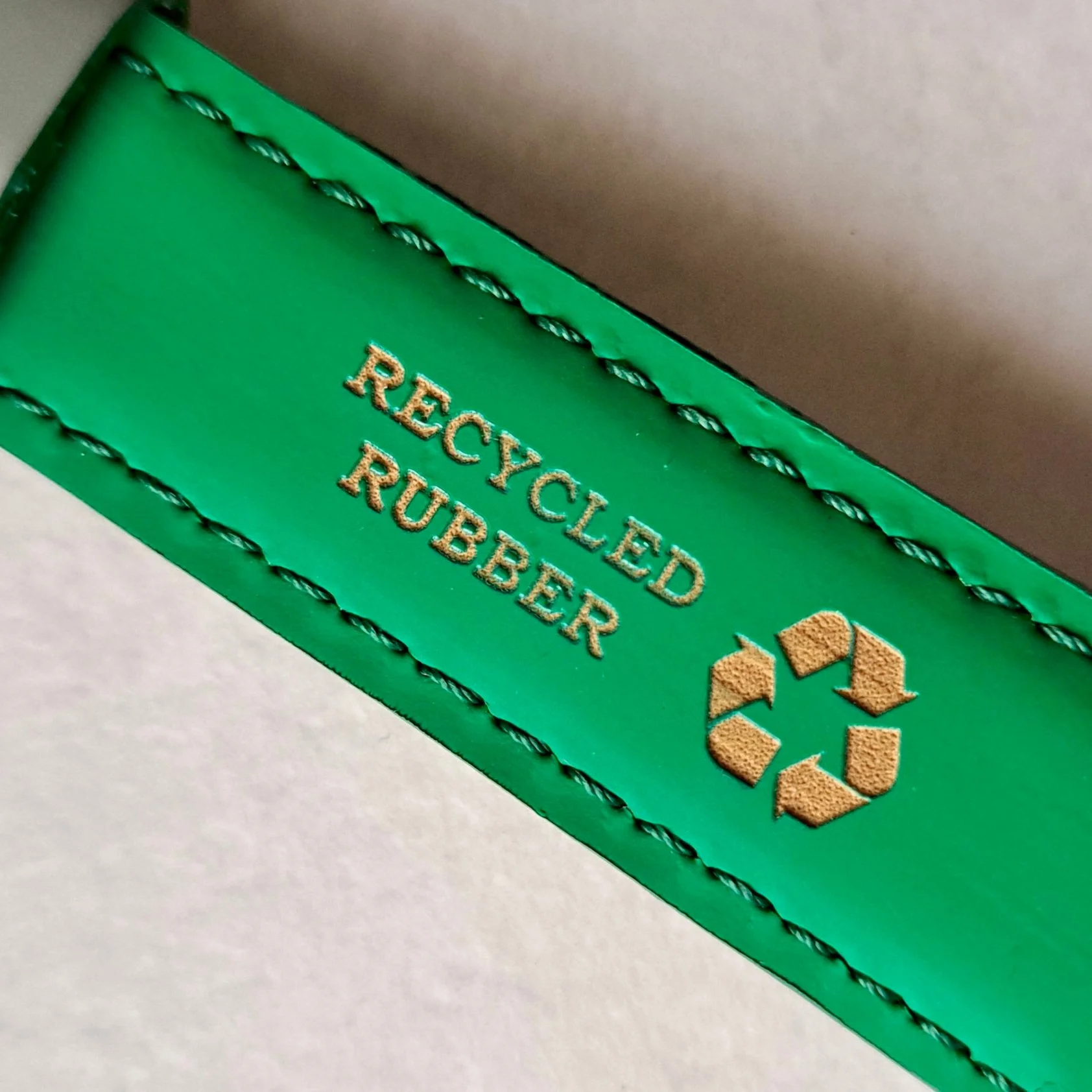 Etichetta verde con il testo dorato 'Recyled Rubber' e un simbolo di riciclo in colore marrone
