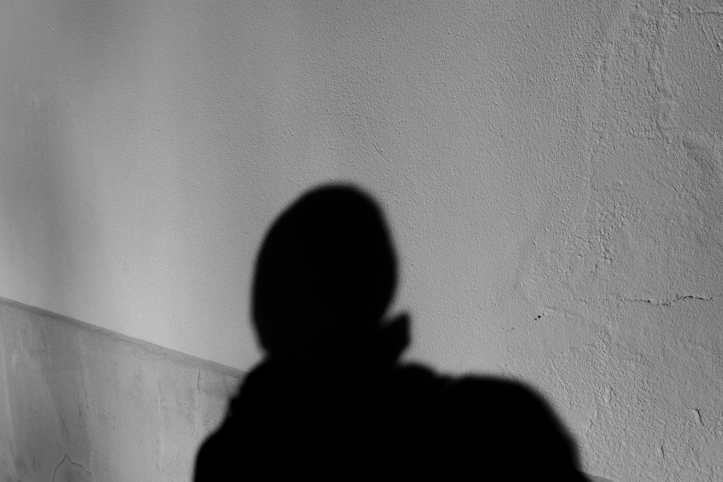 A person's shadow cast on a textured wall, with only the head and shoulders visible in the silhouette.