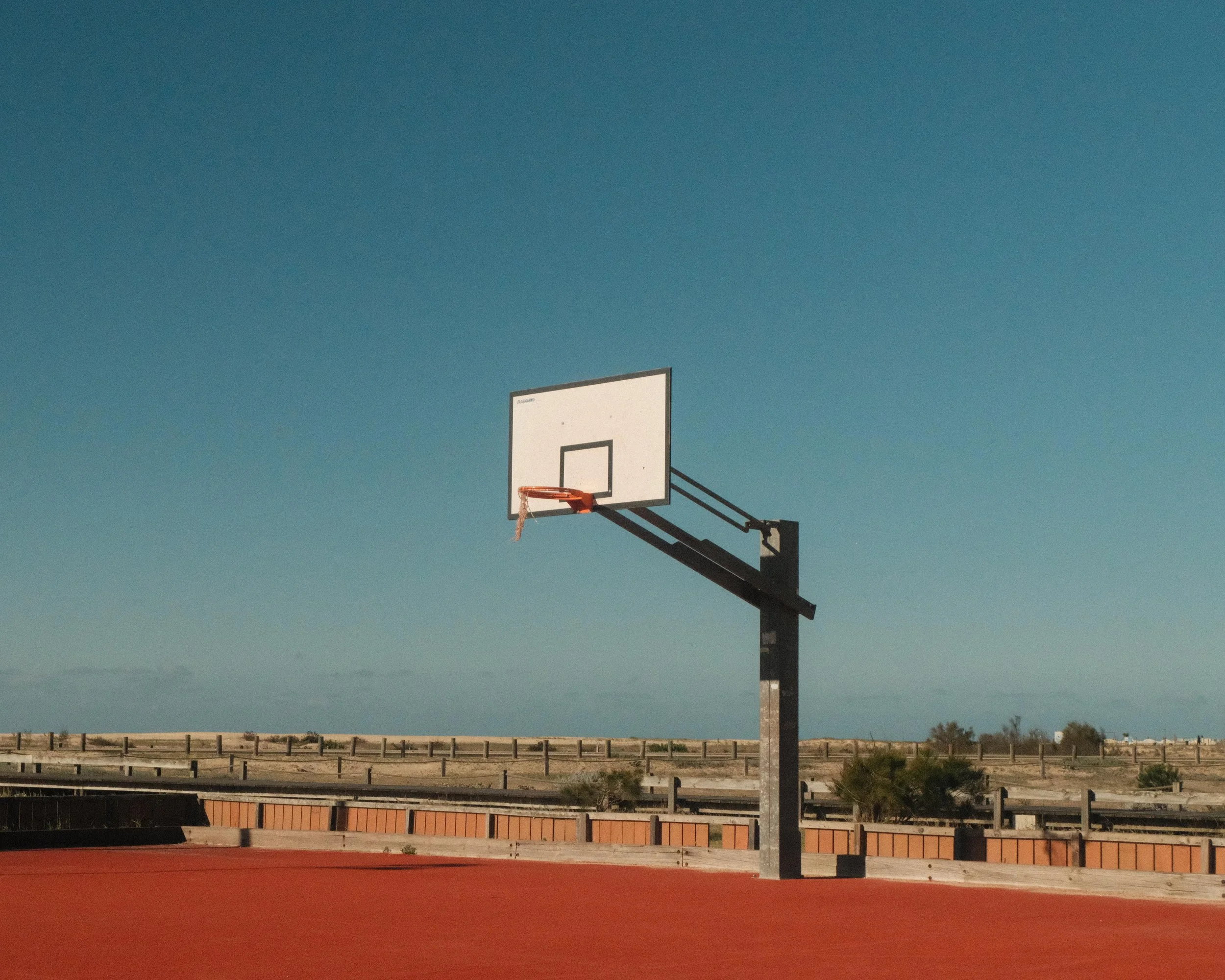 Empty basketball hoop on an outdoor court with a blue sky background.