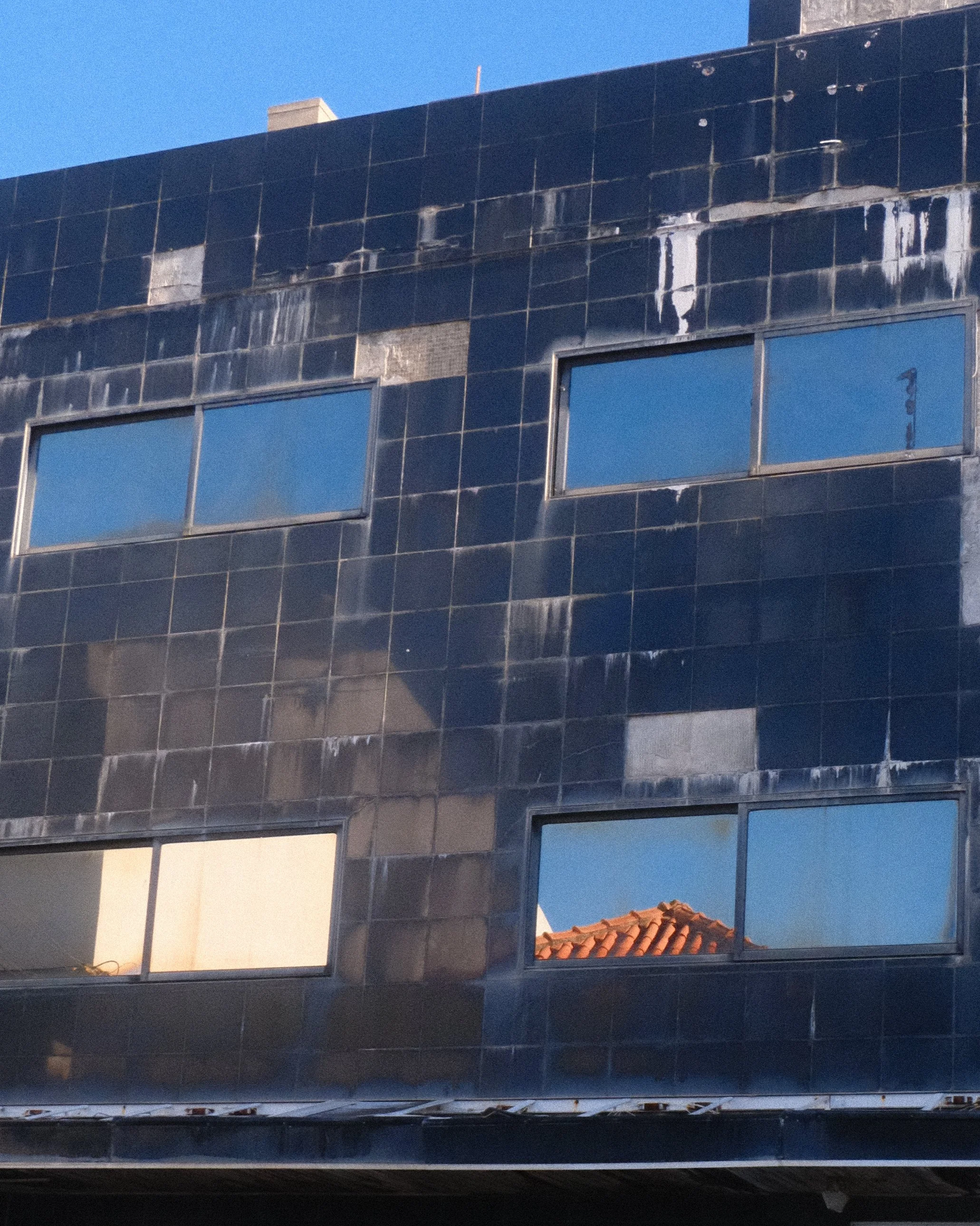A black tiled building with four rectangular windows reflecting the blue sky and a red-tiled roof.