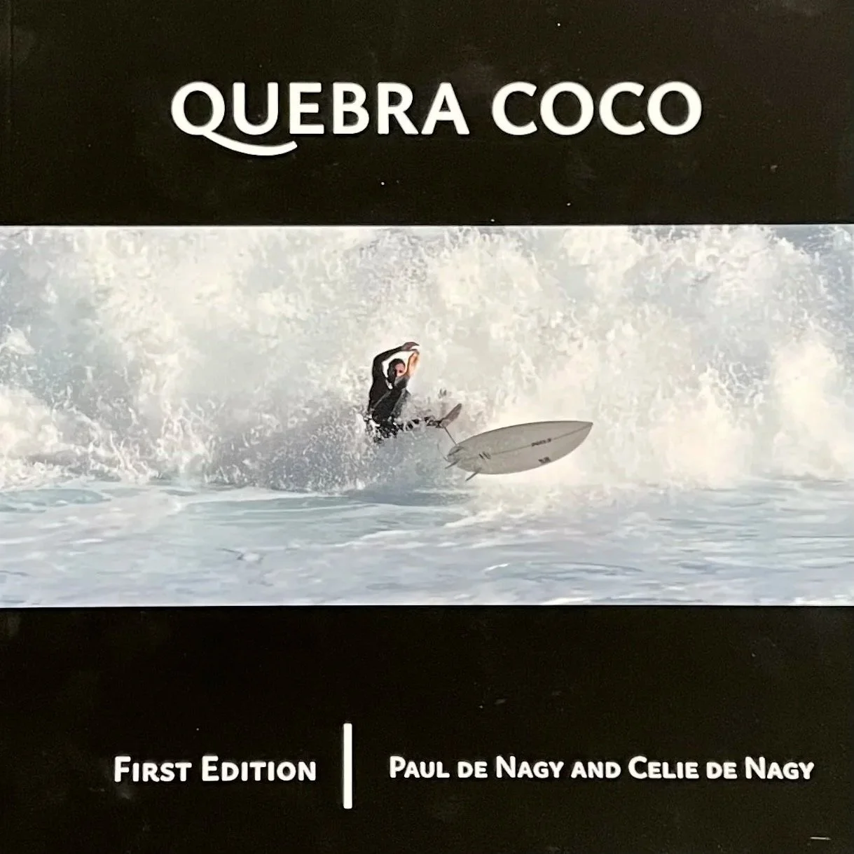 Book cover titled 'Quebra Coco' featuring a person surfing on a wave, with authors Paul de Nagy and Celie de Nagy, labeled as First Edition.