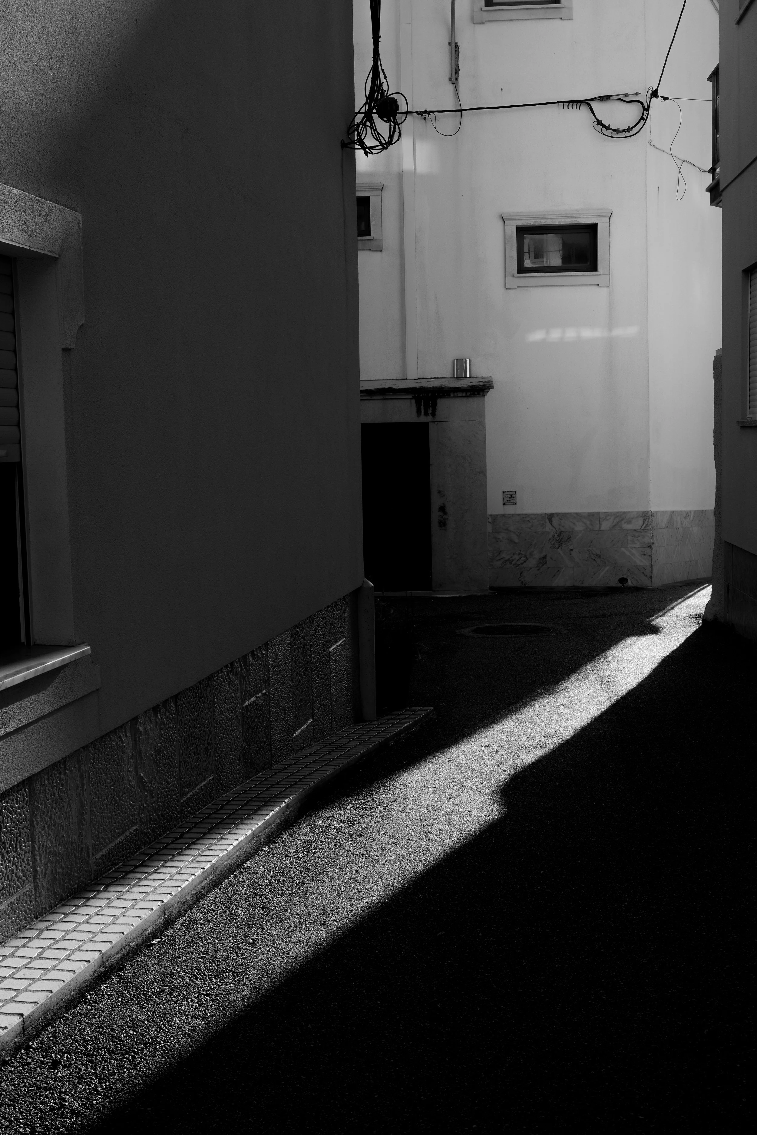 A narrow alleyway between buildings with dark shadows and bright light illuminating part of the ground.