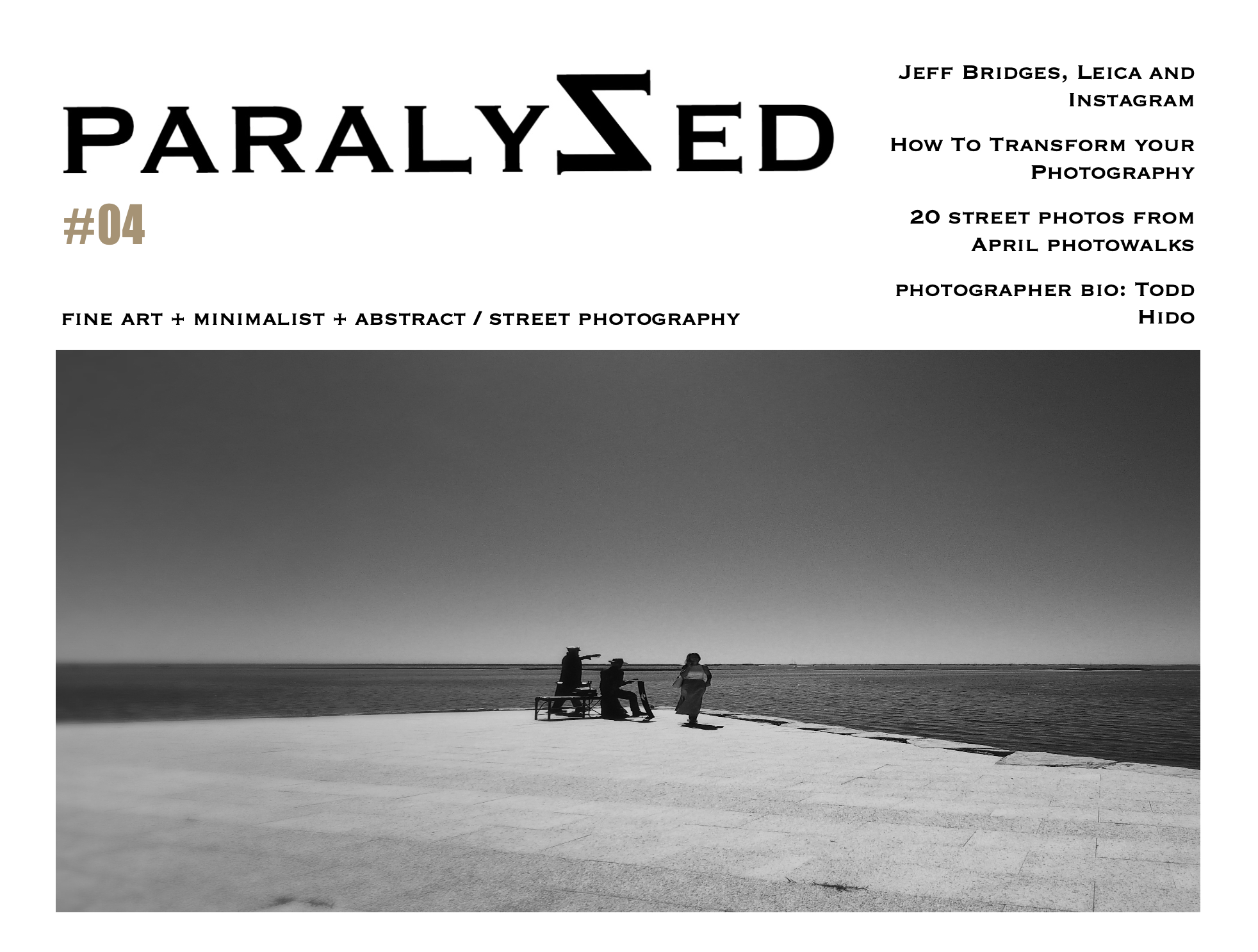Black and white photo of three people on a beach, two sitting on a bench and one walking, with a large body of water and a horizon line in the background.