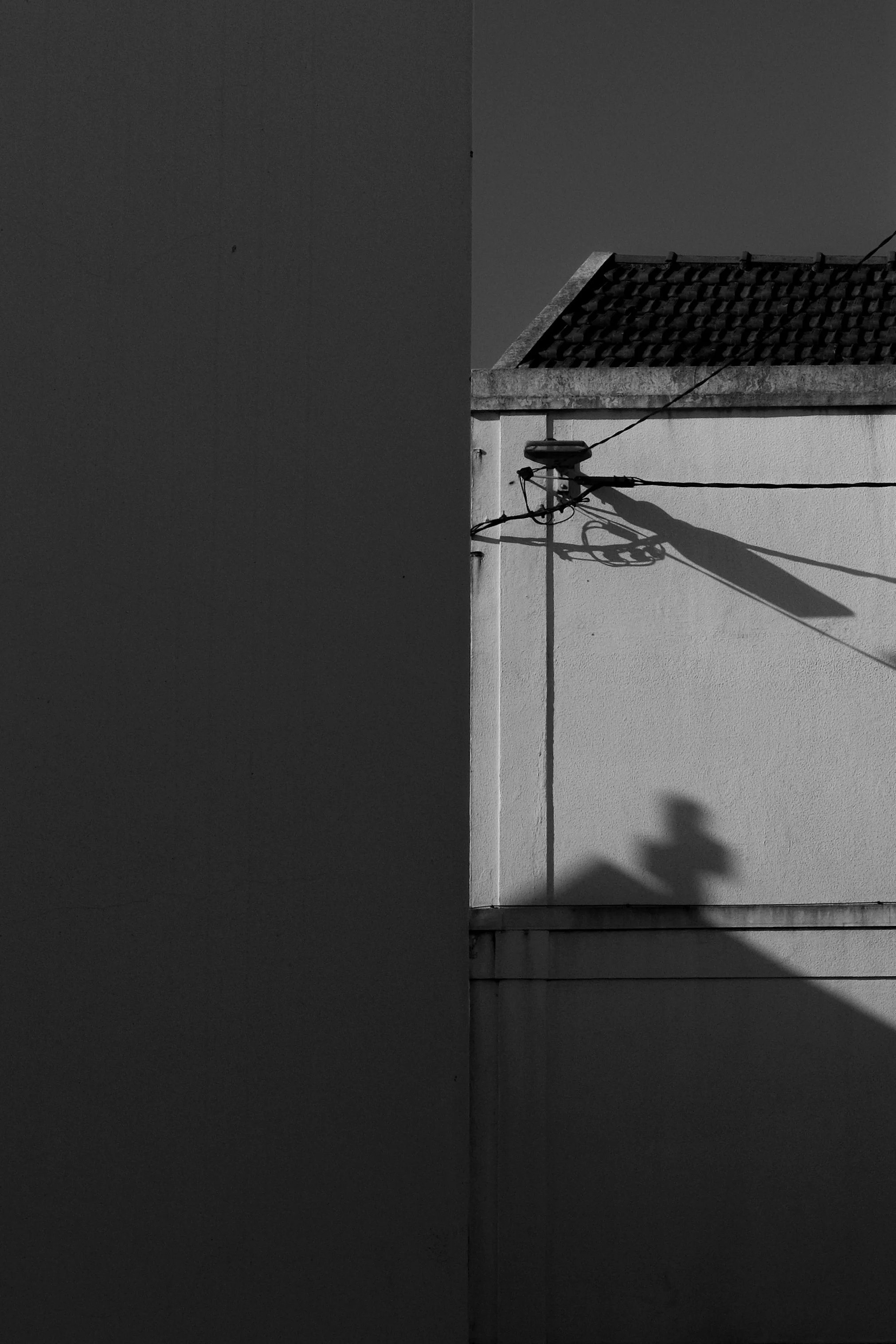 A black and white photo of a wall with electricity wires and a shadow of a street sign cast on it.