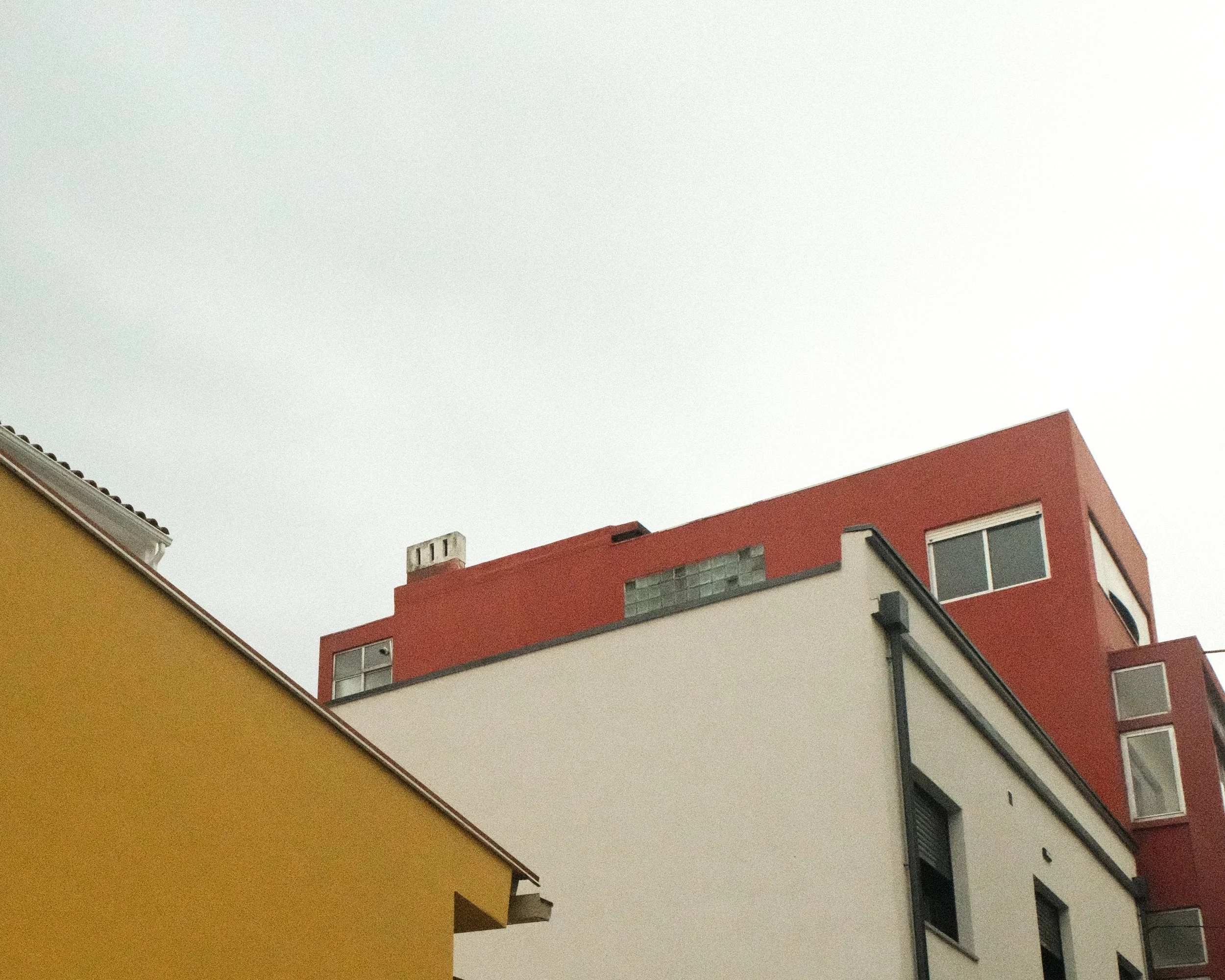 Low-angle view of white, yellow, and red buildings against an overcast sky.