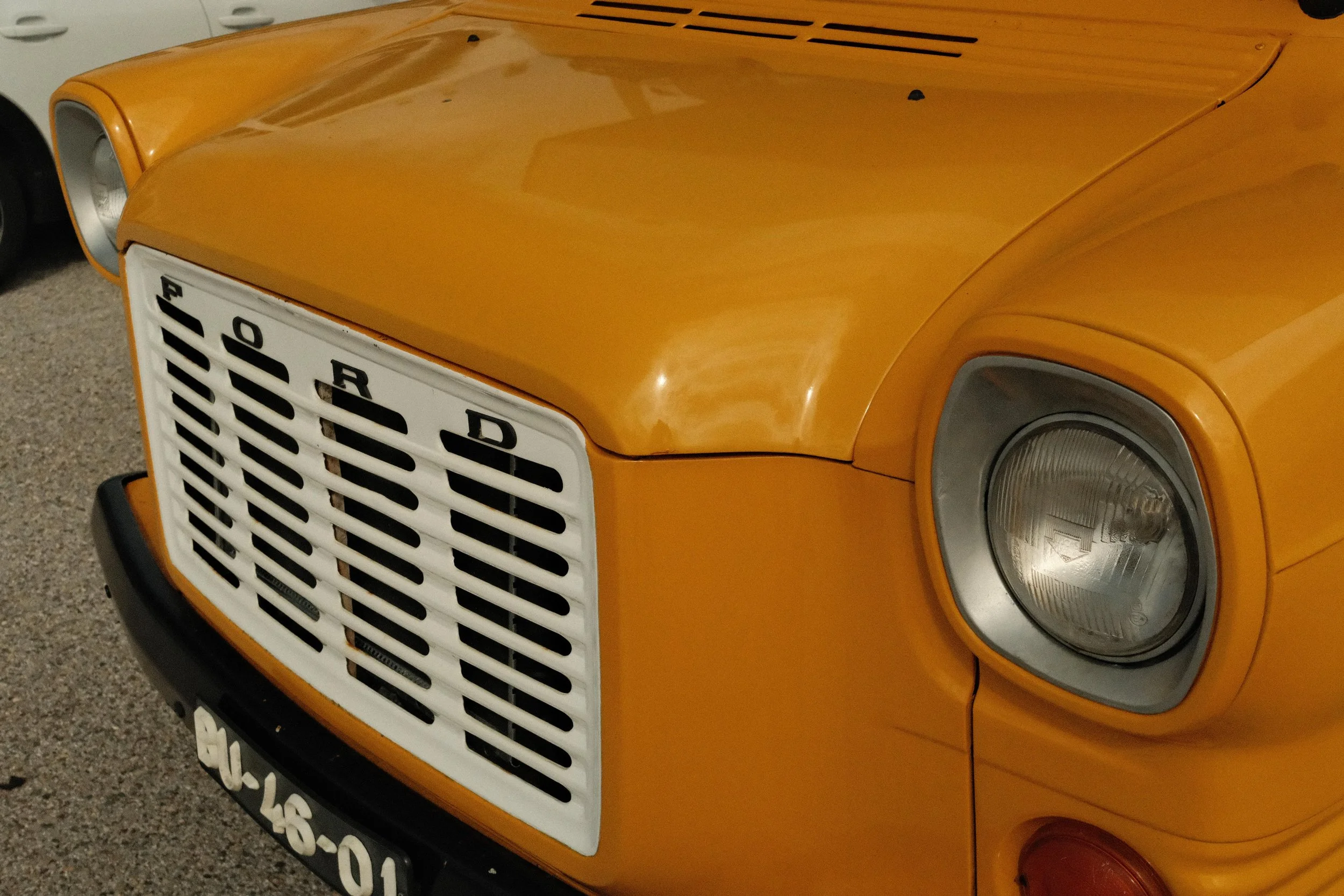 Front of a vintage yellow Ford car with a white grille, round headlight, and a black bumper.