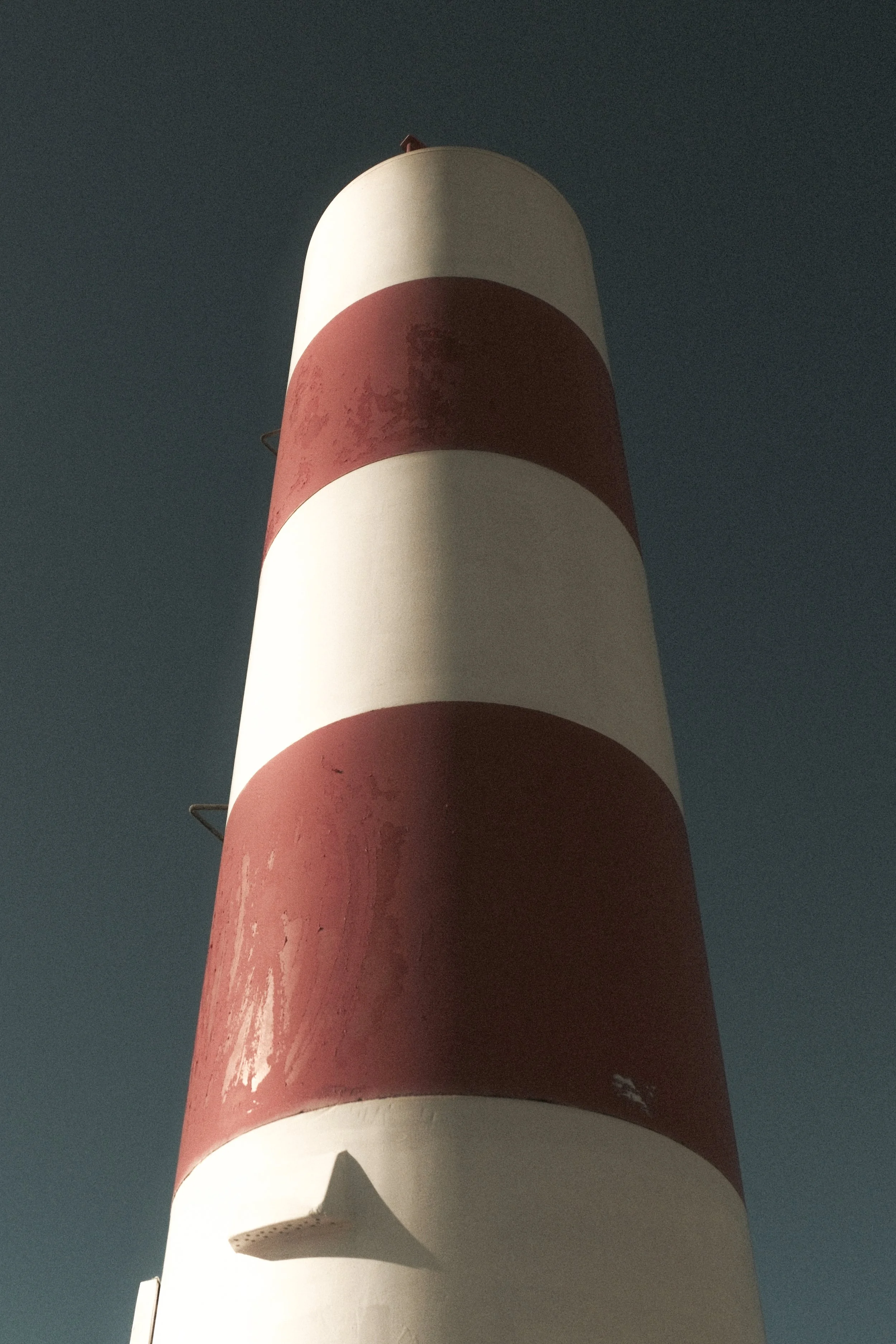 A tall lighthouse with red and white horizontal stripes against a clear sky.