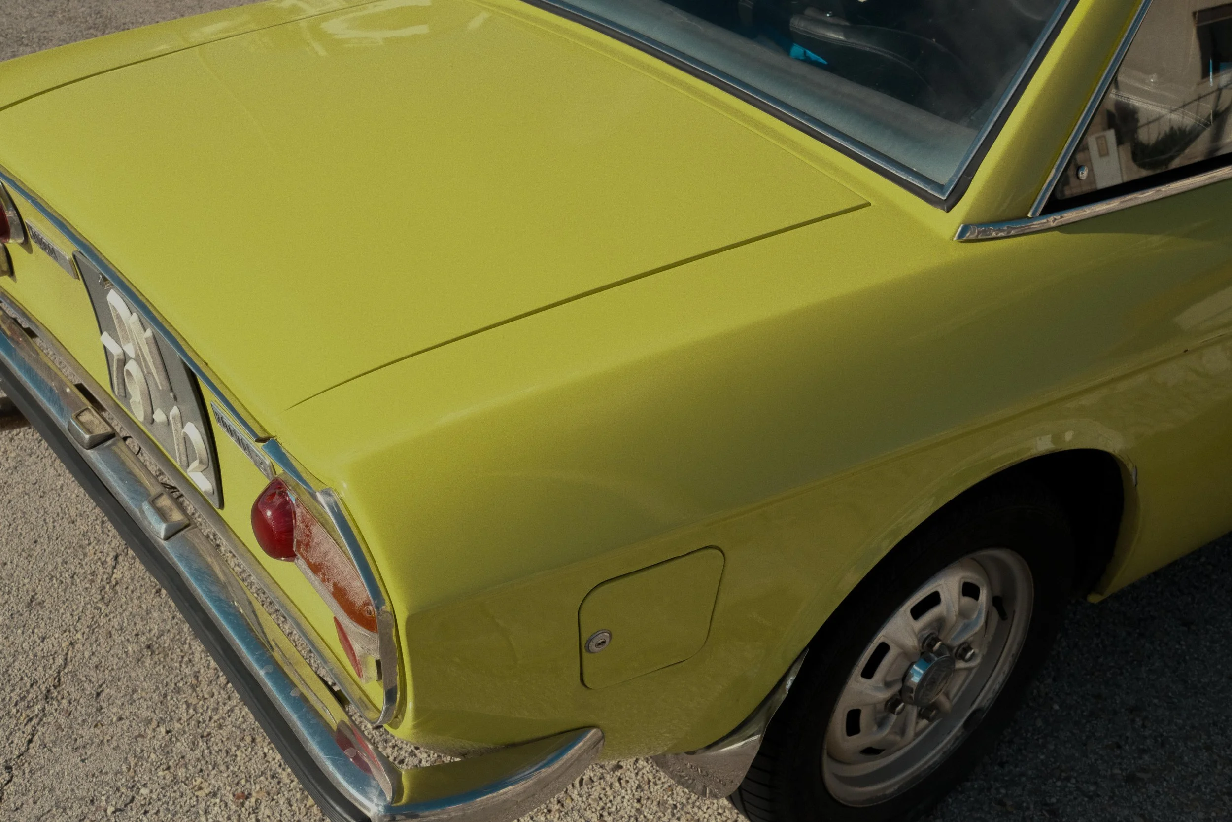 Close-up of the rear corner of a vintage green Dacia car, showing tail light, trunk, and rear wheel.