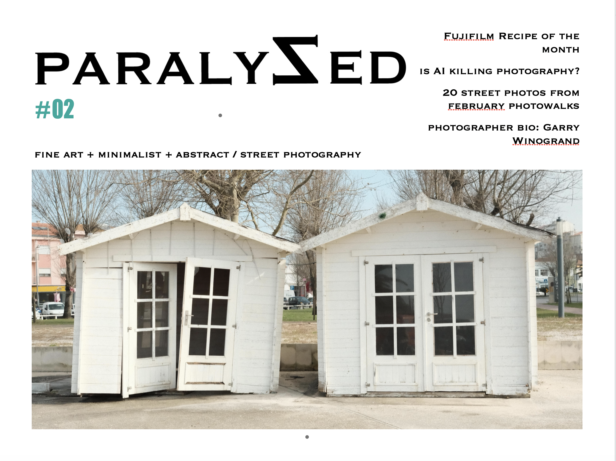 Two small white wooden houses with glass-paneled doors, one tilted slightly, situated outdoors on pavement with leafless trees in the background.