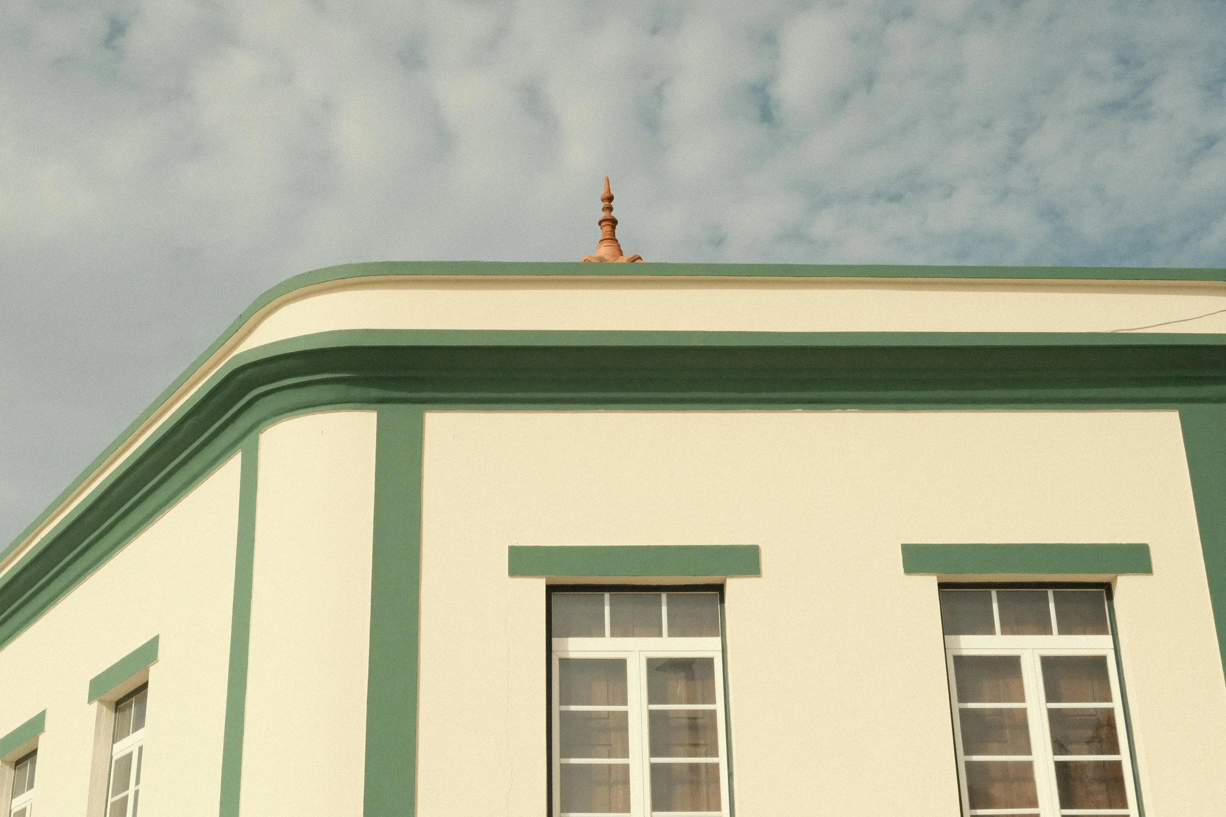 Close-up of a building with a green and cream facade and two windows, under a cloudy sky.