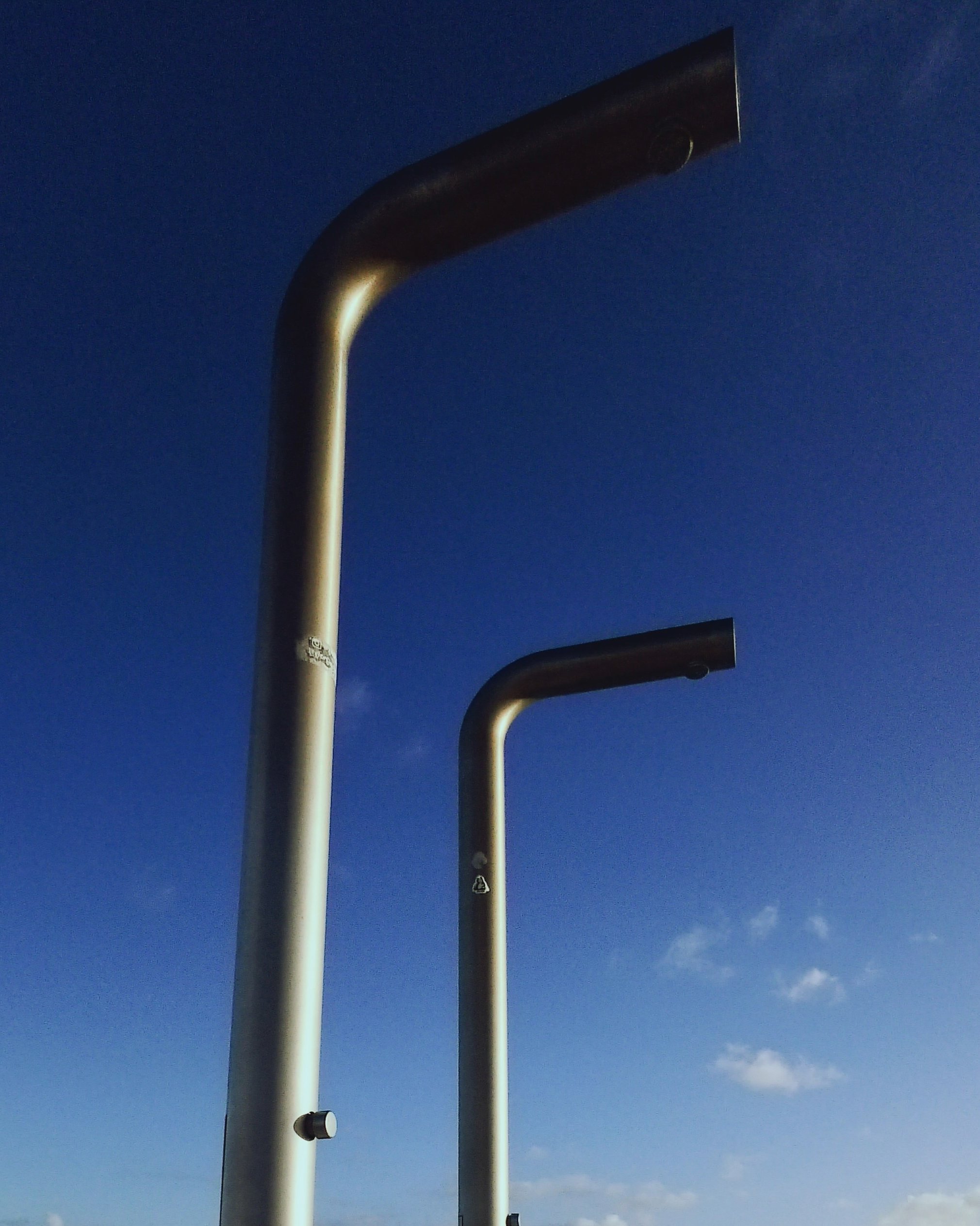 Two large metal drinking water fountains with spouts facing downward against a clear blue sky.