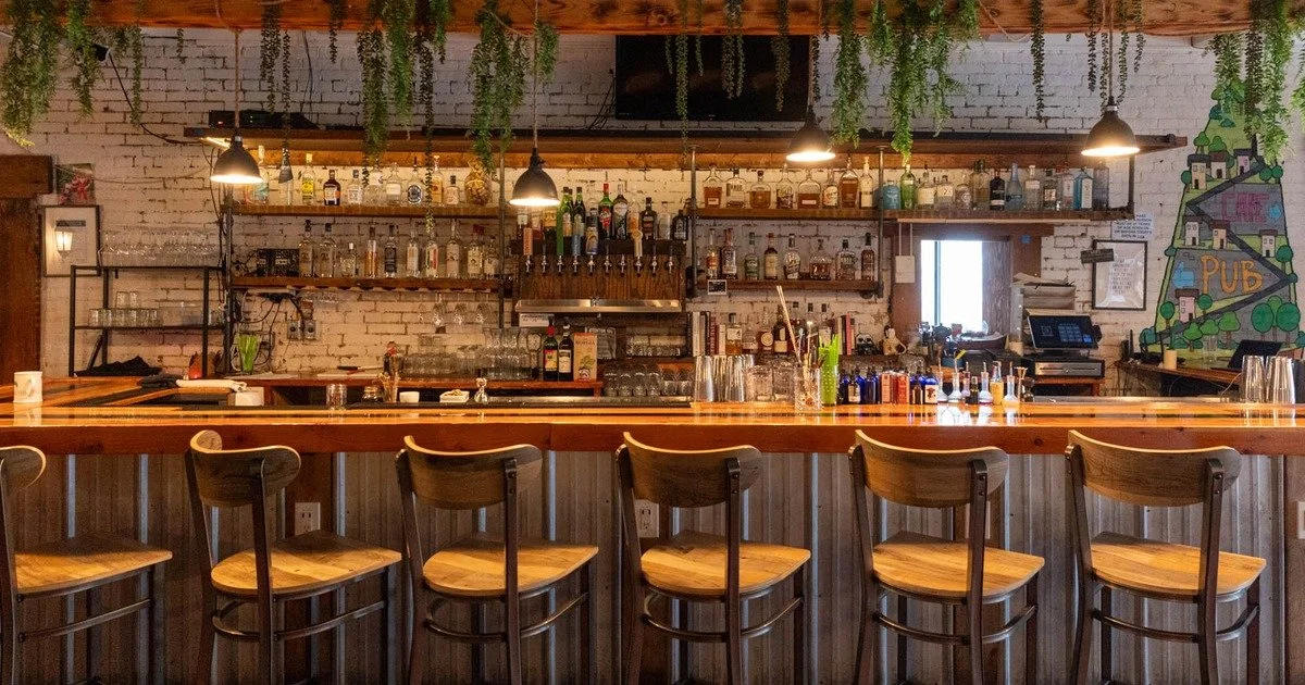 The bar at Scratch and Co., wooden counter, bottles on shelves, warm hanging lights
