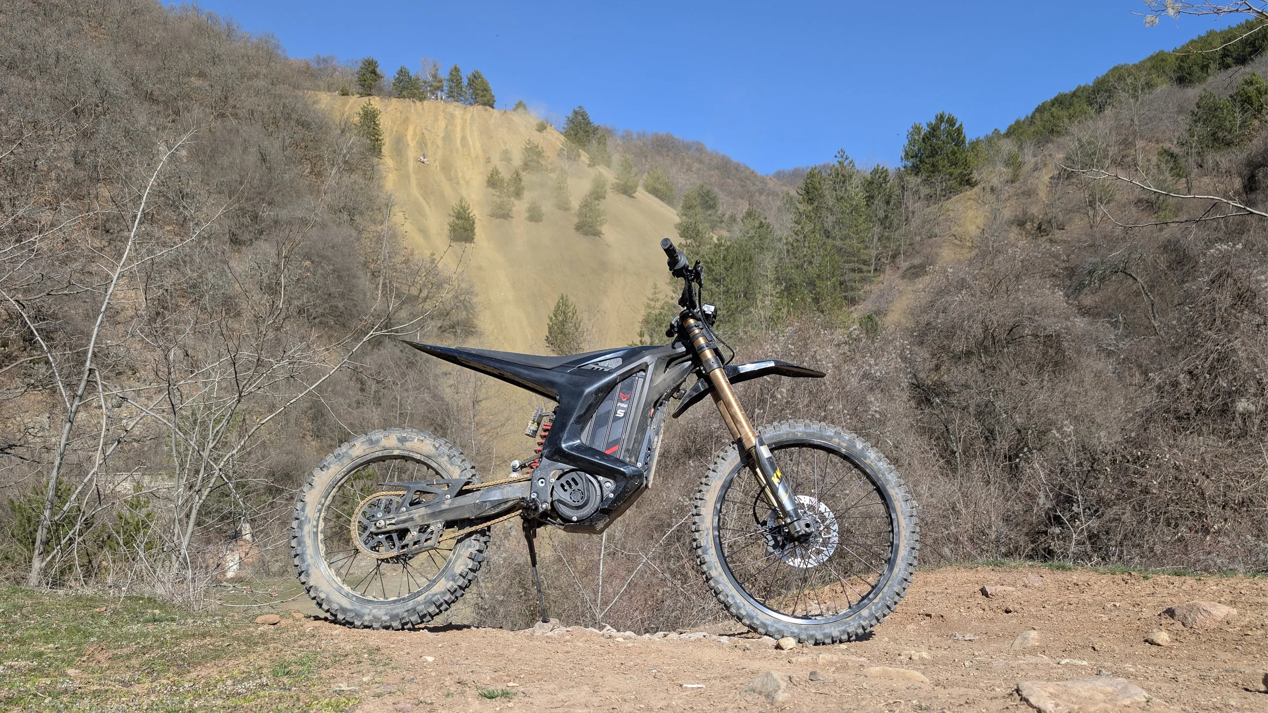 Electric mountain bike on a dirt trail with a hillside covered in trees and a clear blue sky in the background.