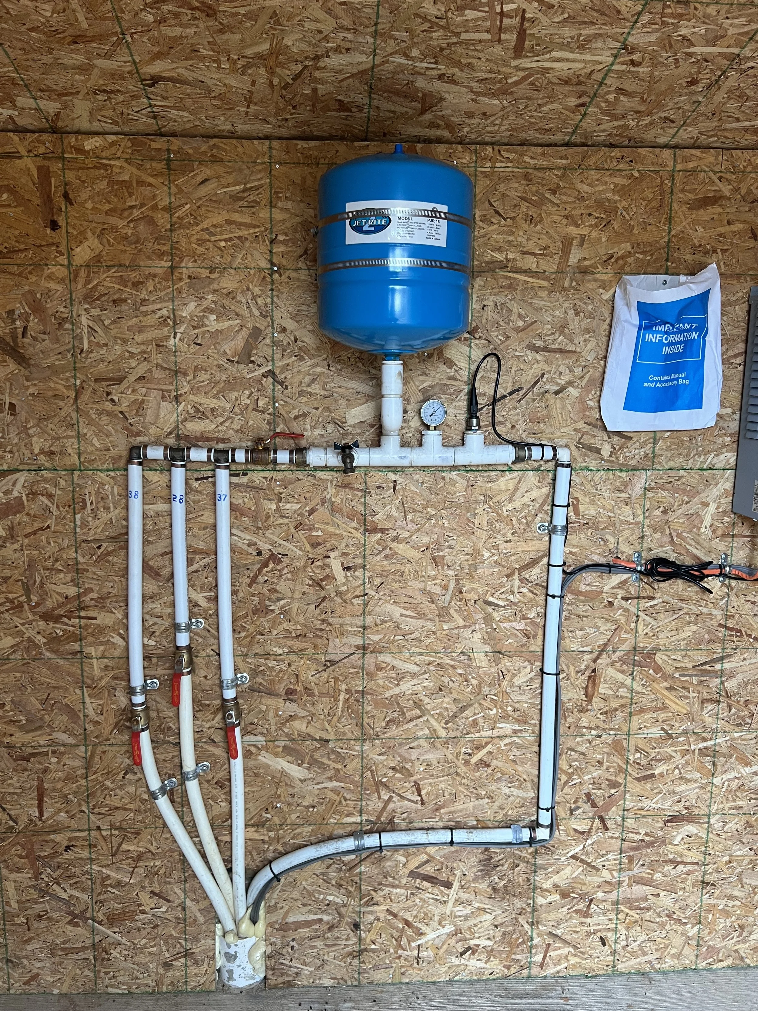 Piping system with gauges and a blue expansion tank mounted on an OSB wall, used for water filtration, Cary Plumbing, pipe installation, Raleigh plumbing, plumber near me, licensed plumber, drain repair, gas water heater replacement, repair plumber