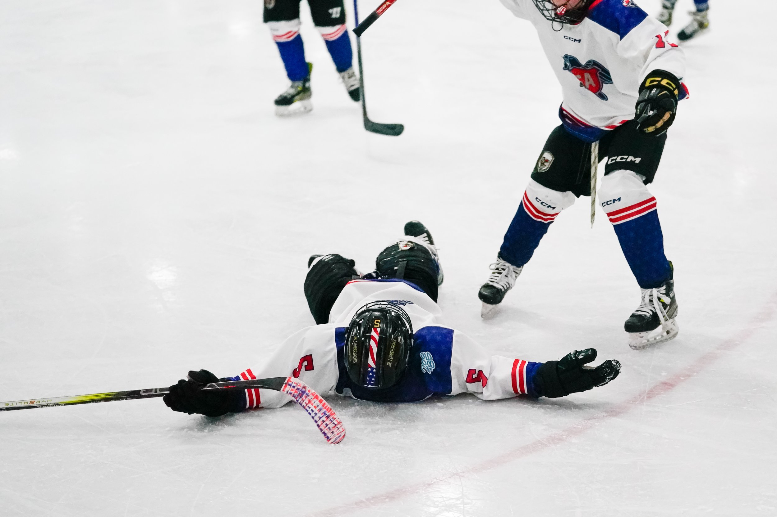 Hockey player lying on ice rink during game with teammates nearby.