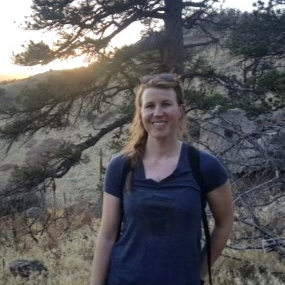 Woman with a backpack outdoors in a forested area during sunset.