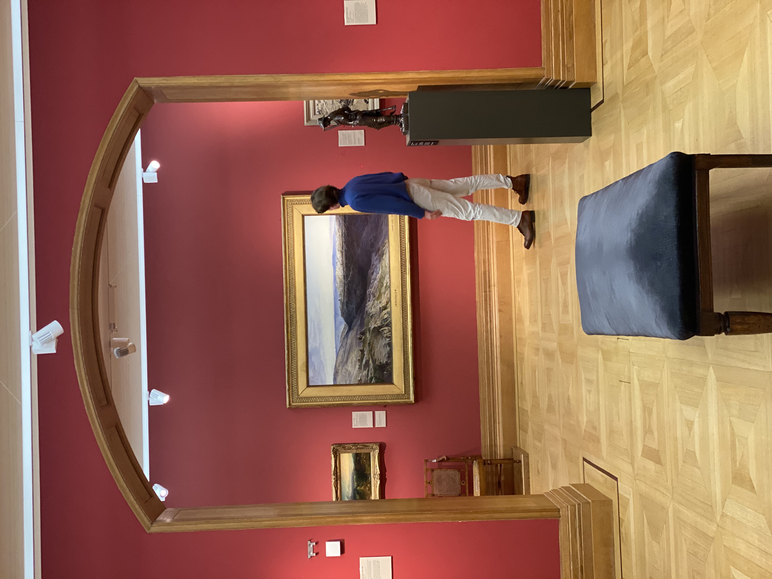 A person looking at artwork in a gallery with red walls and wooden floors.