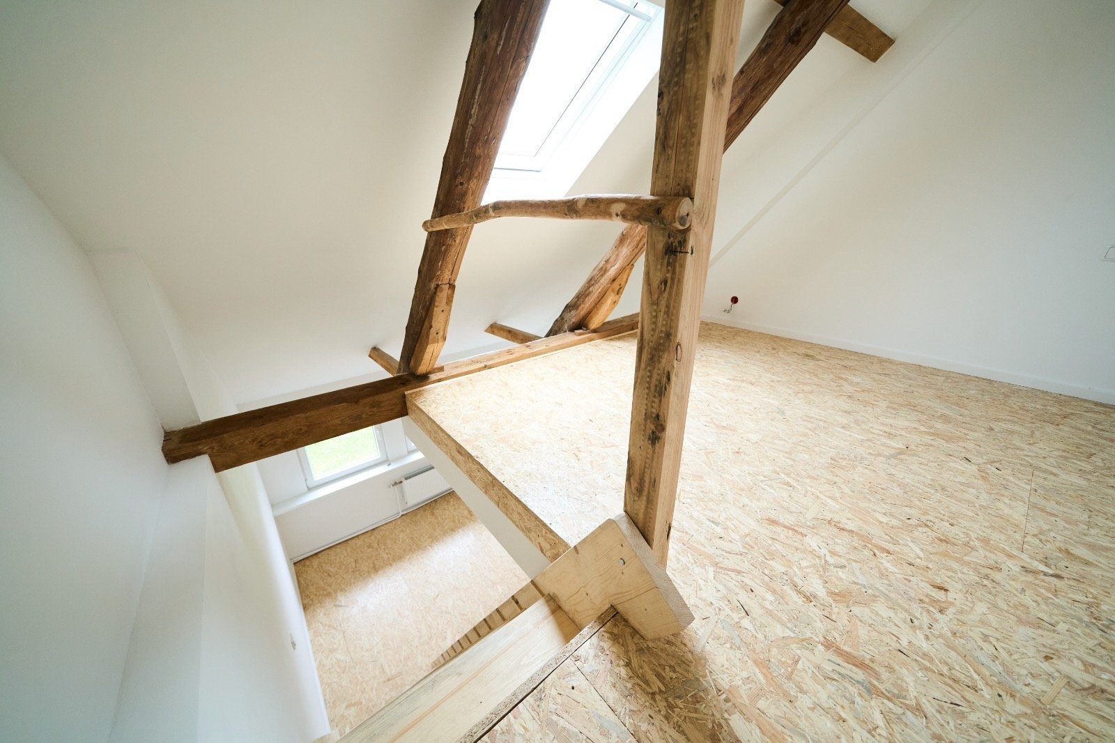 Innenansicht eines Dachbodens mit sichtbaren Holzträgern und einem Oberlichtfenster. Der Boden besteht aus OSB-Platten.