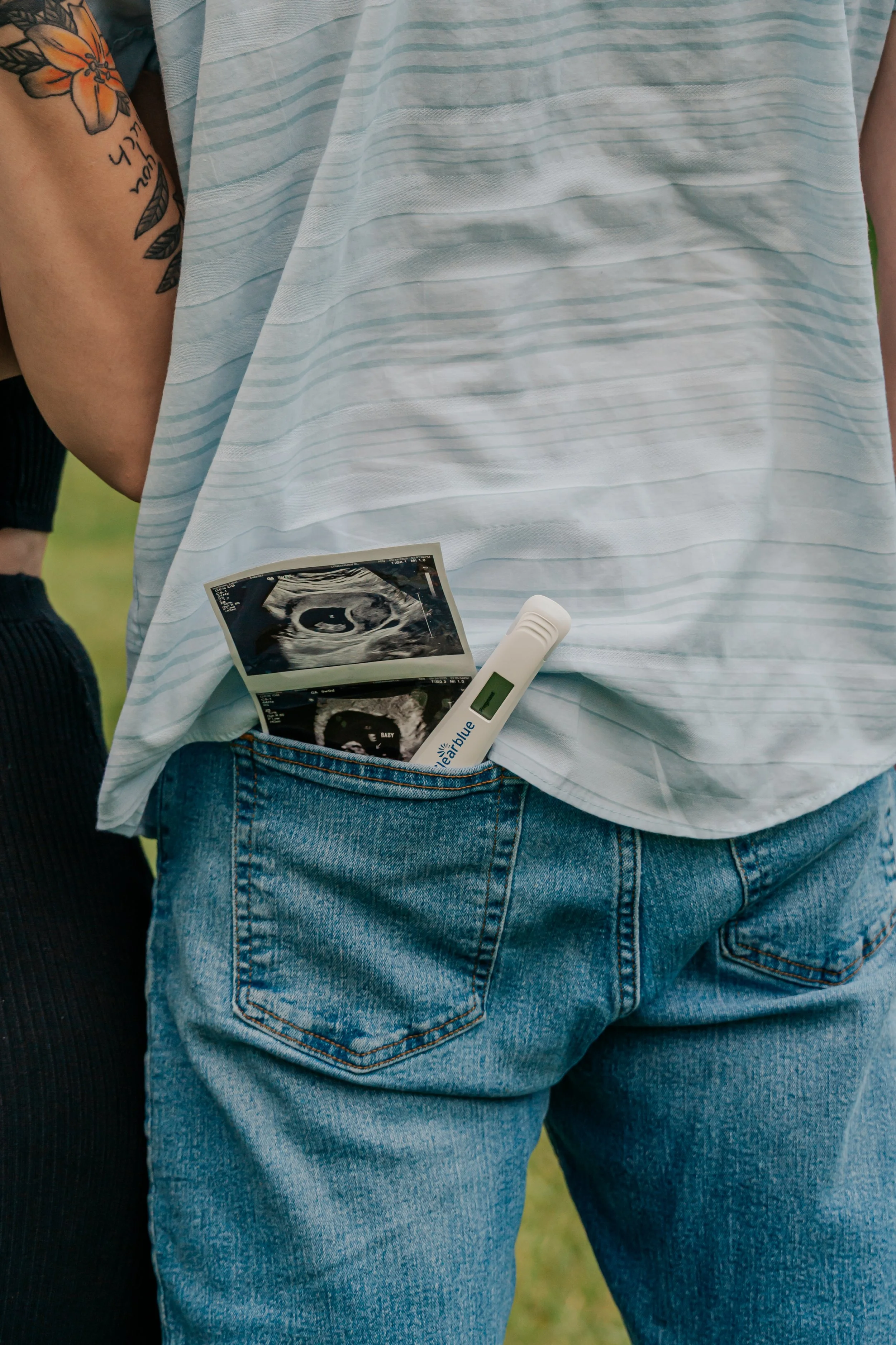 Person wearing a white striped shirt and blue jeans with ultrasound photos and a pregnancy test in their back pocket.