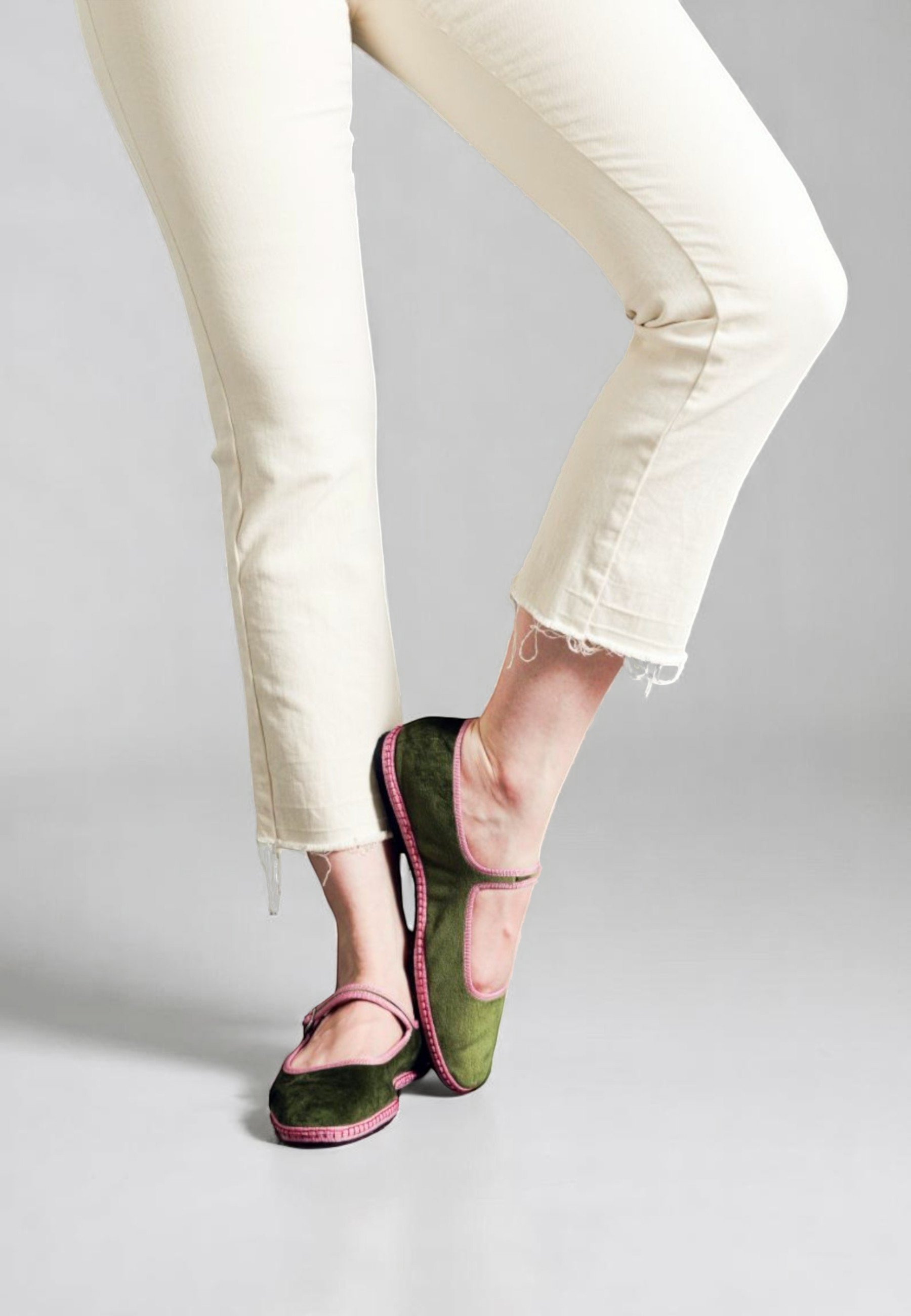Playful pose with lifted foot, model wearing Italian velvet Mary Jane slippers, forest green with pink accents