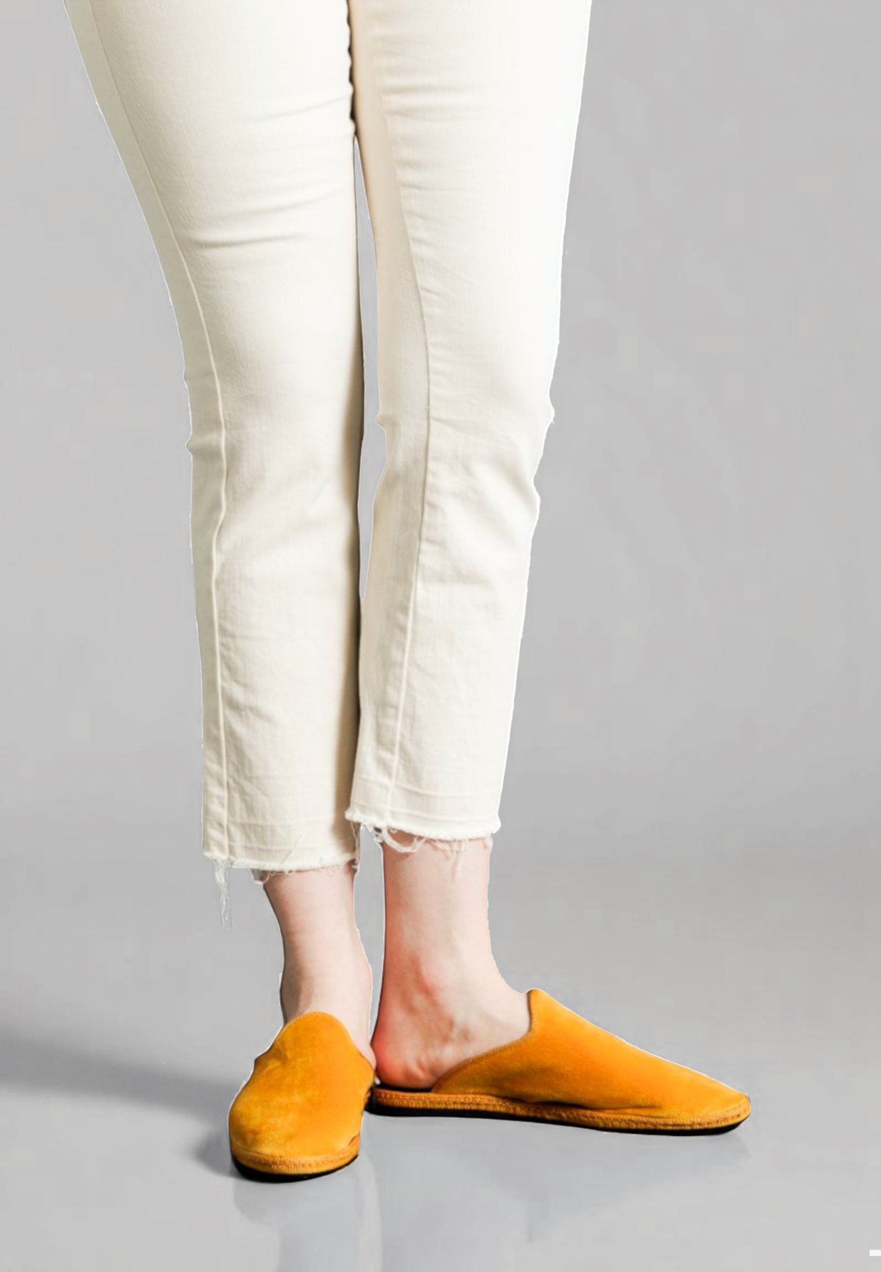Front view of model in rich Sole yellow velvet mules with distressed hem jeans