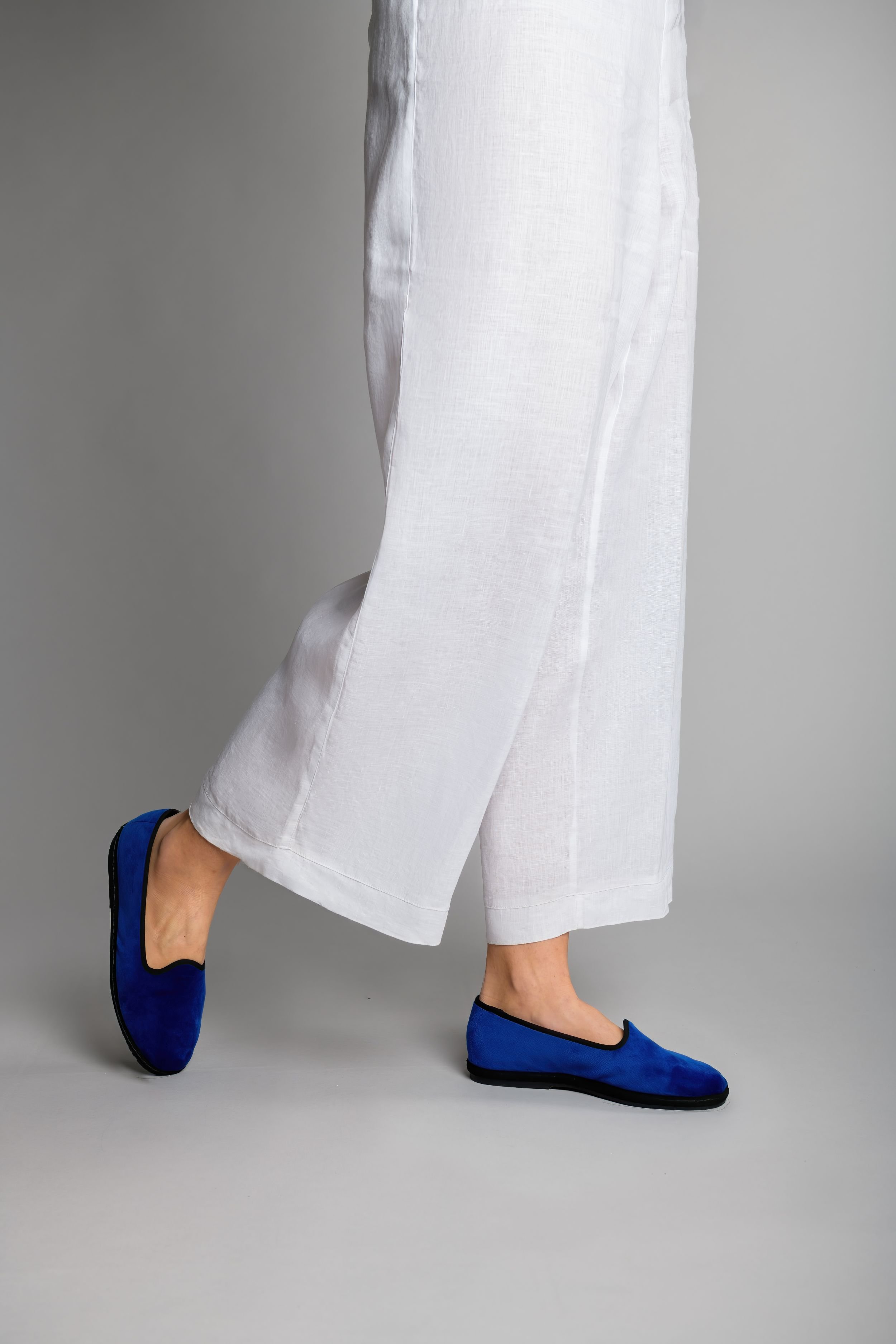 Side walking view of Gioia velvet slippers styled with white pants