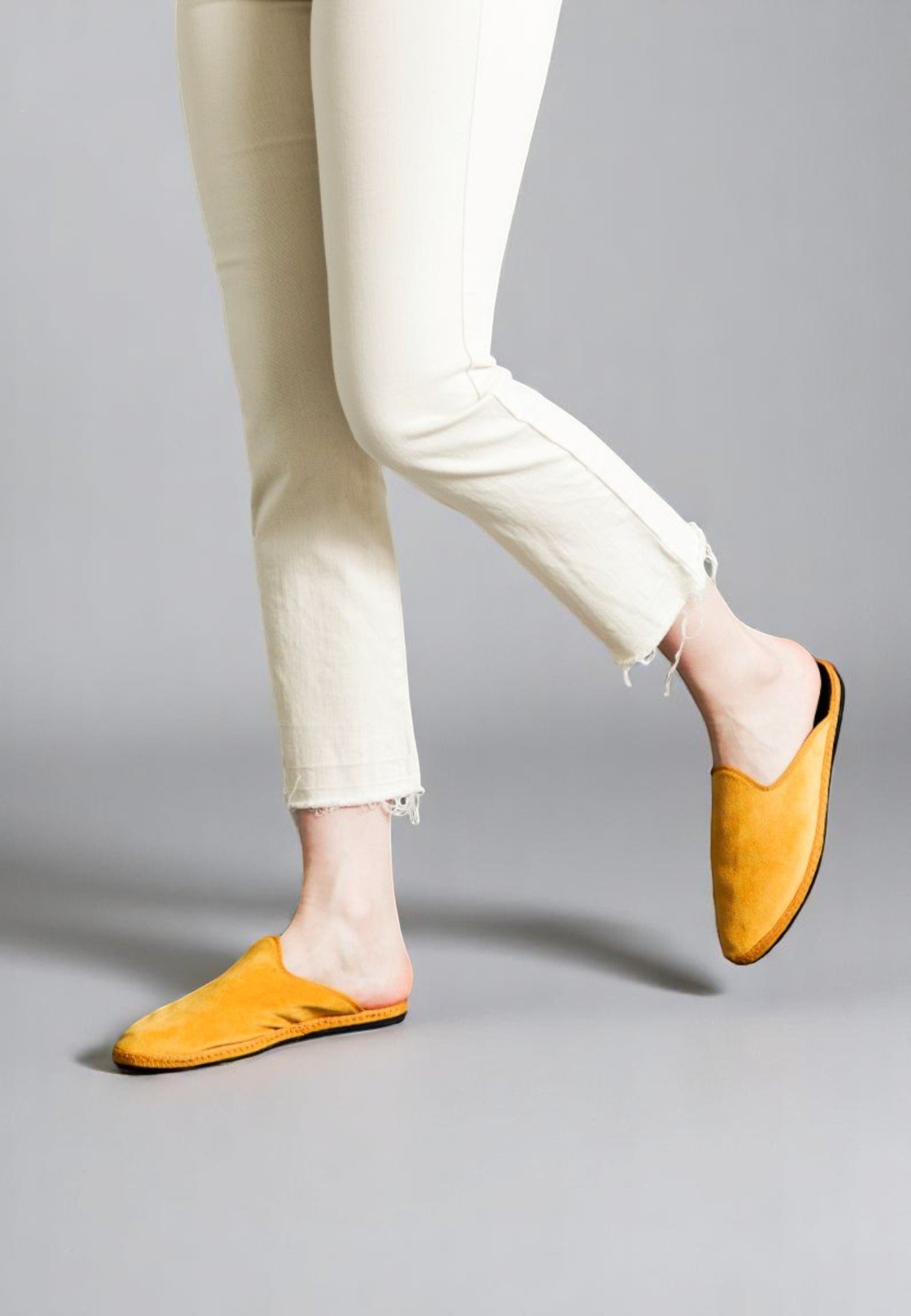 Walking motion of model in golden yellow velvet Solea slides, styled with cropped ivory pants