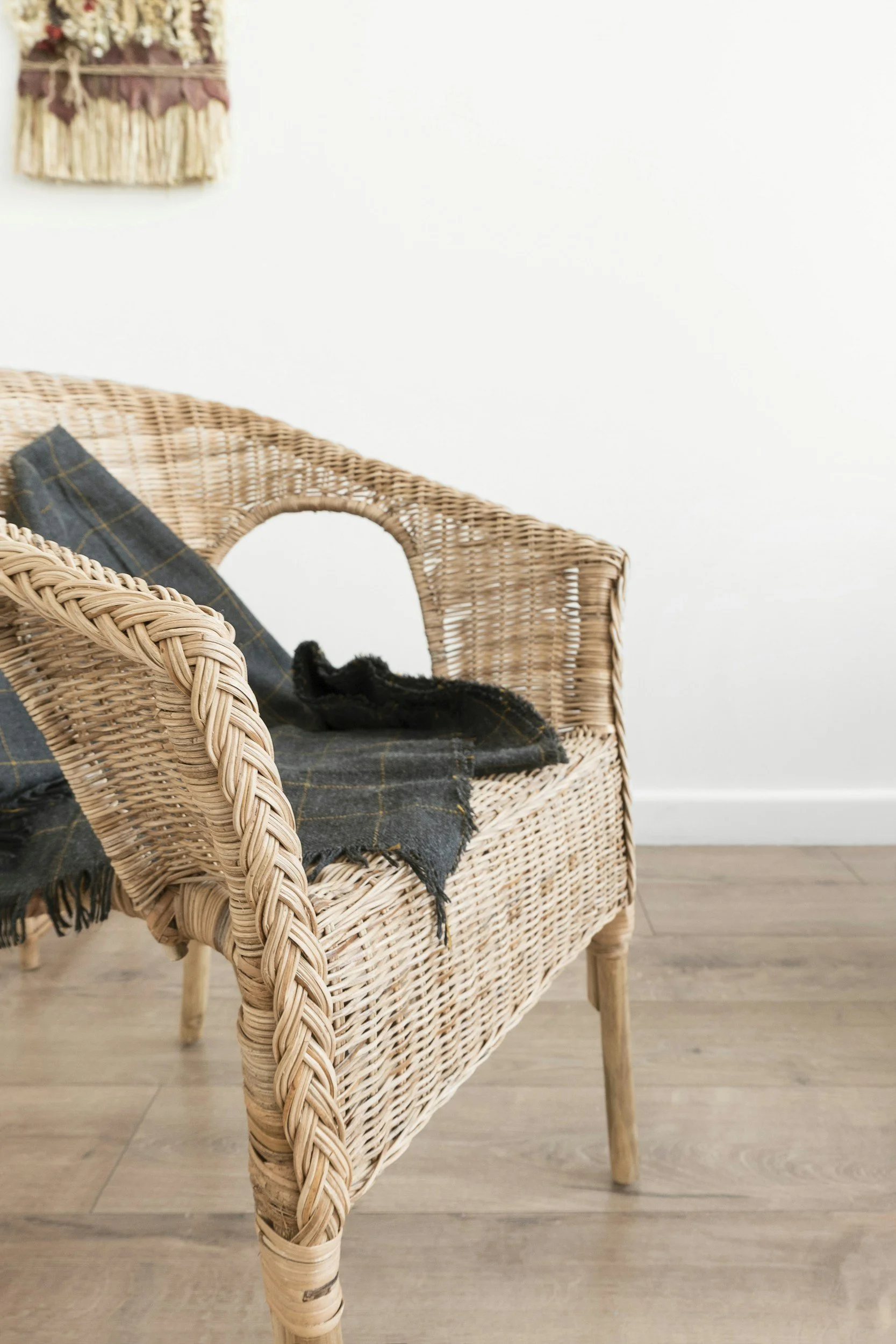 Close-up of a wicker chair with a black and yellow plaid blanket draped over it, set against a white wall.