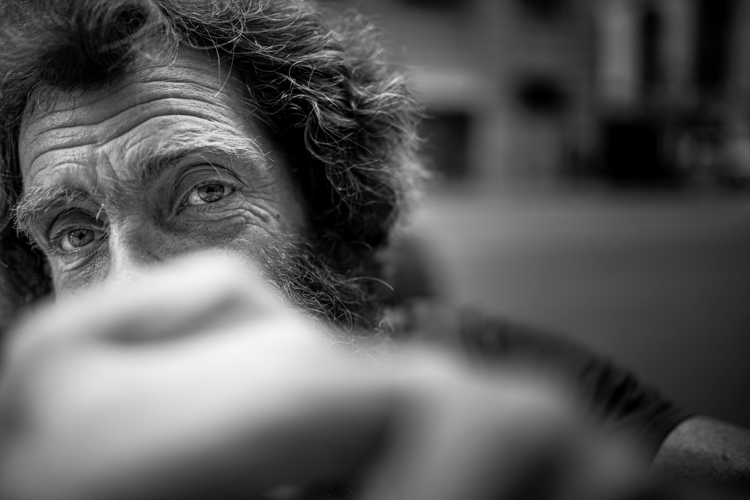 Close-up black and white portrait of an older man with curly hair and facial hair, focusing on his eyes.