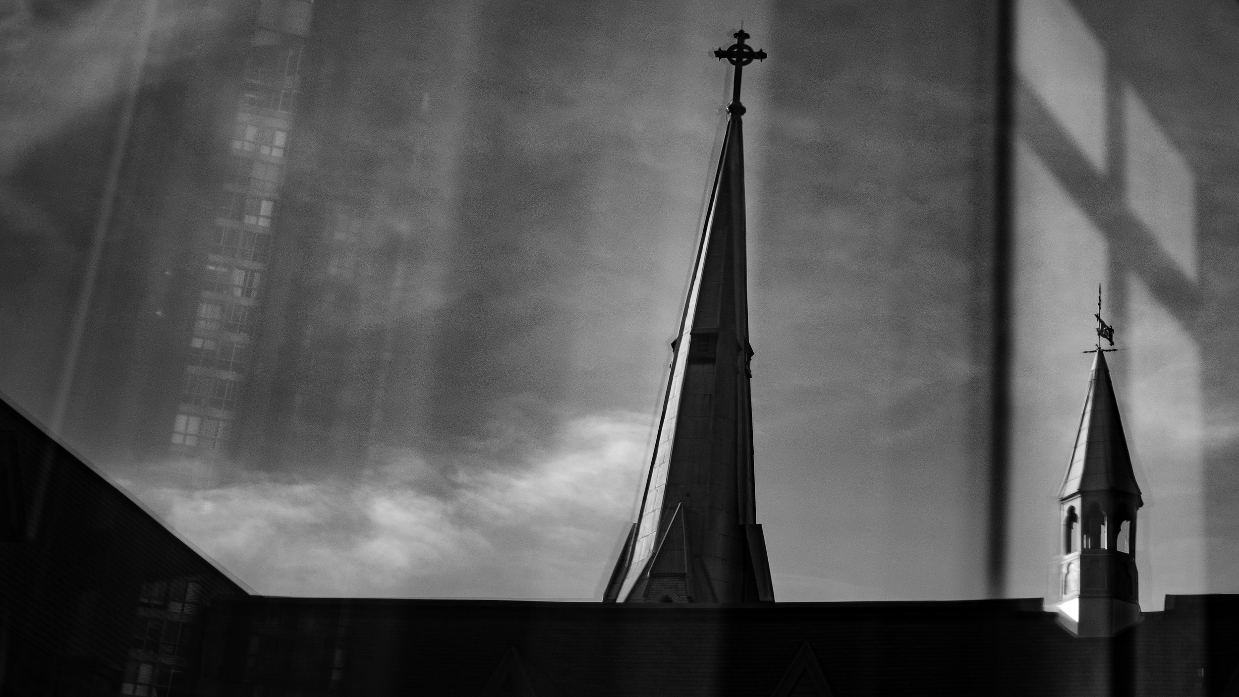 Silhouette of church steeples with reflections on a glass building, black and white photograph.