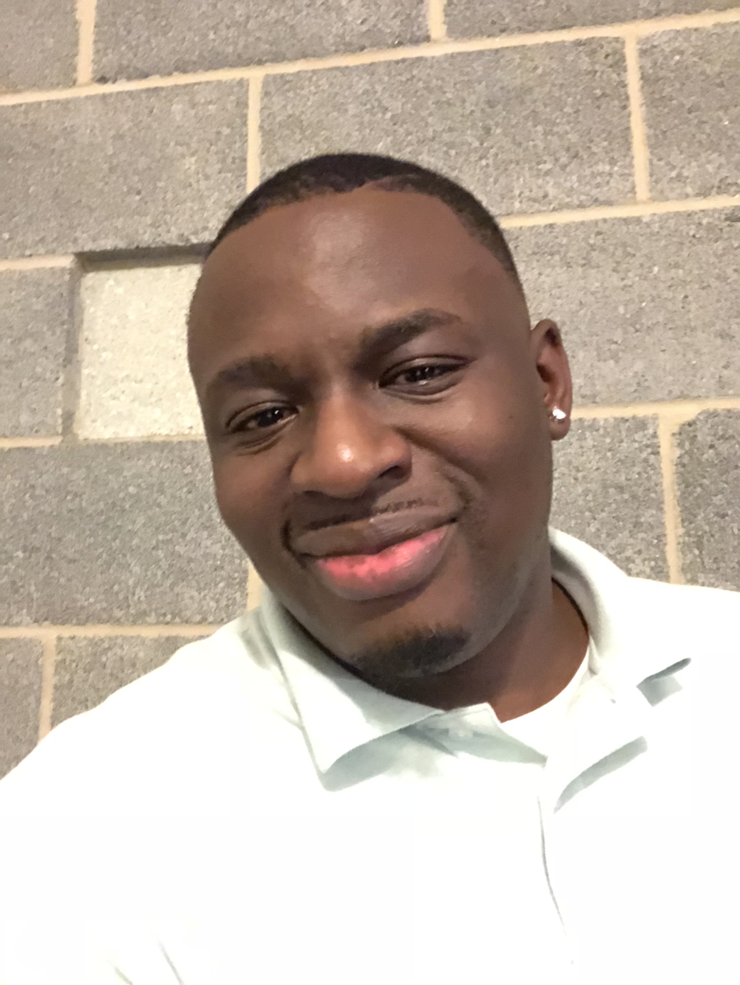 Person smiling in front of a cinder block wall, wearing a light-colored polo shirt.