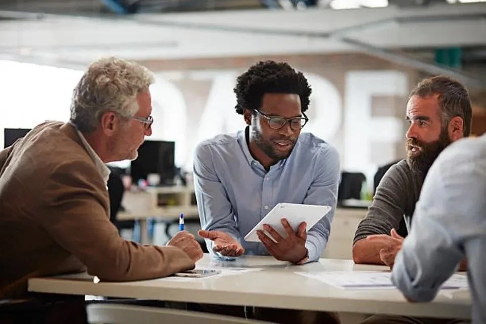 Three men having a business meeting, one holding a tablet, at a modern office table.