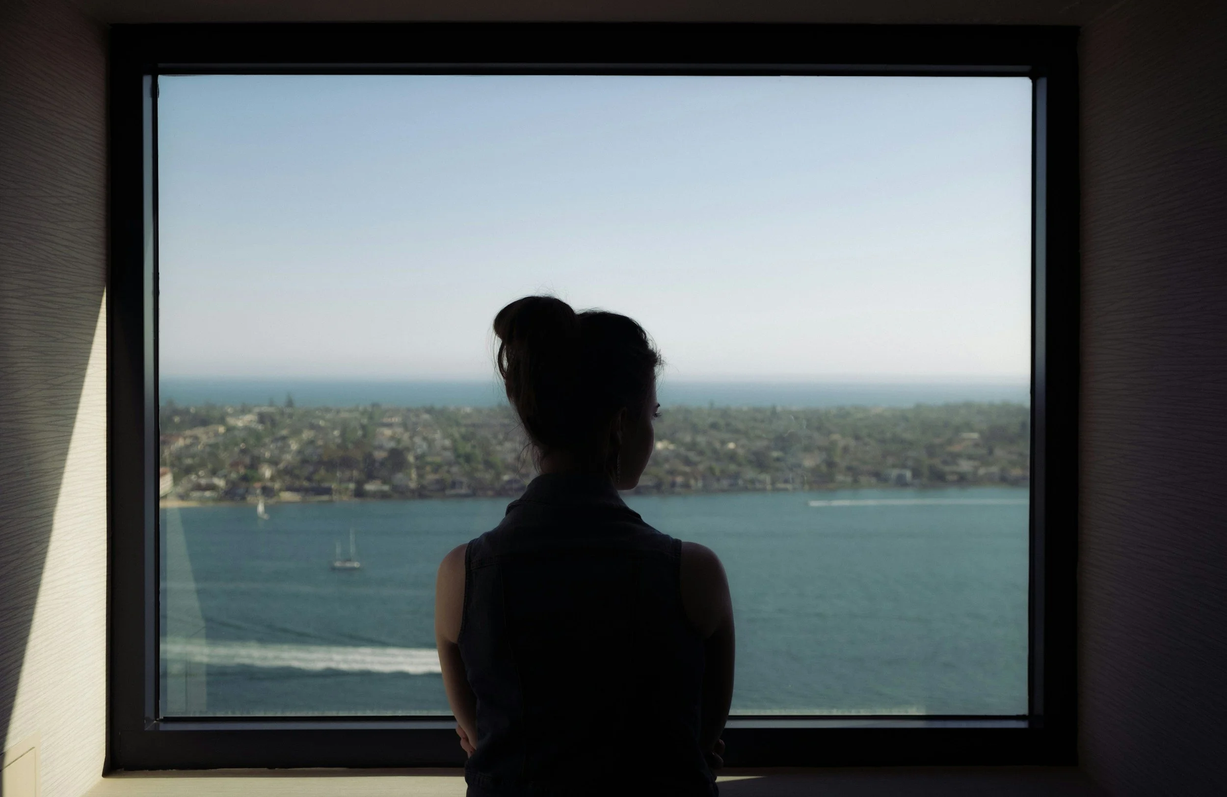 Silhouette of a woman in Texas looking out a window over a cityscape and ocean view.