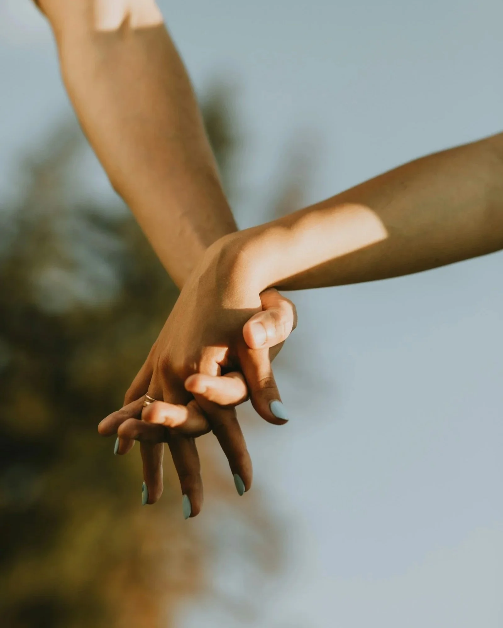 Two hands, one darker and one lighter, are intertwined against a blurred outdoor background.