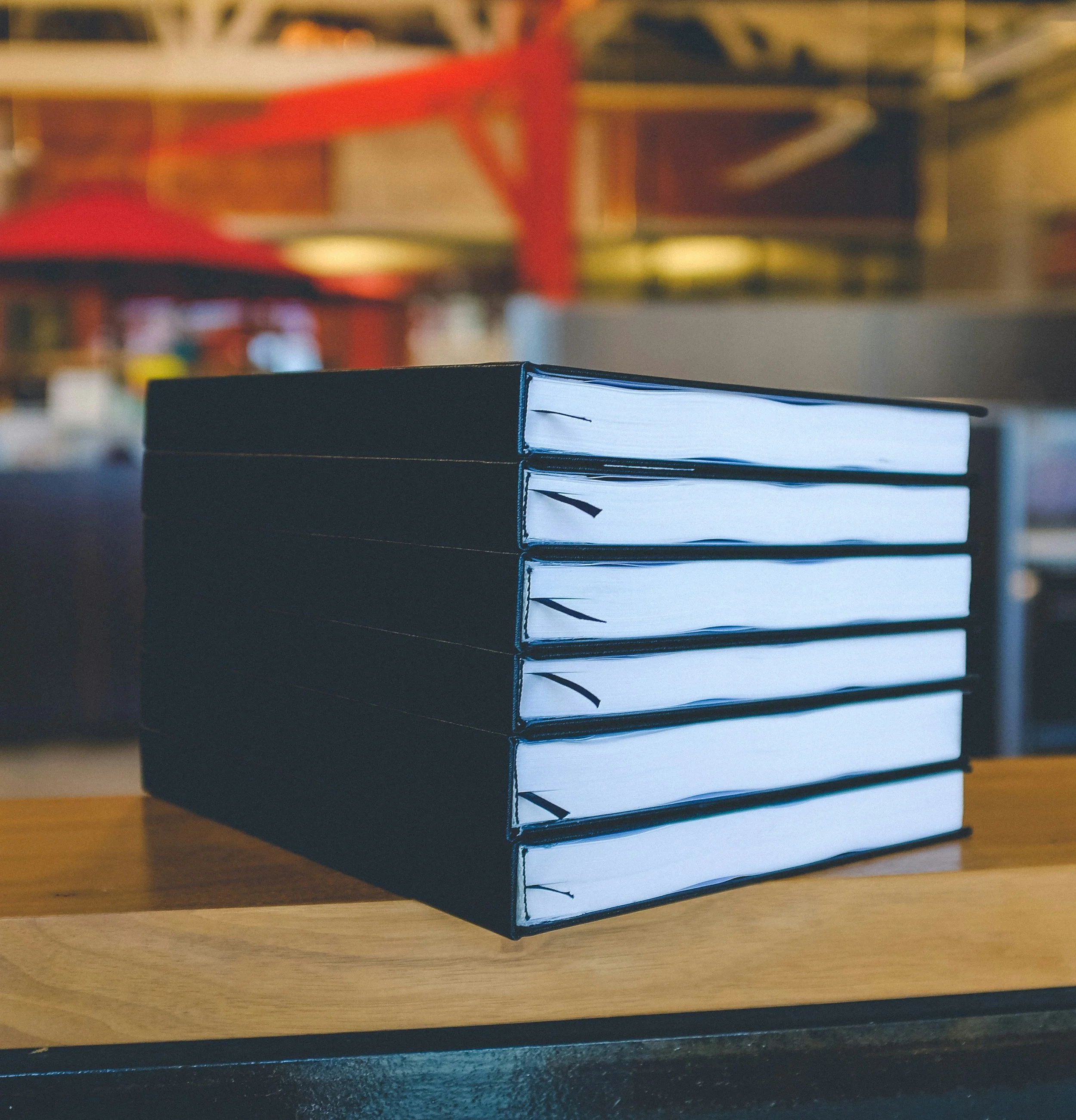 Stack of five black hardcover books on a wooden surface in a blurred indoor setting.