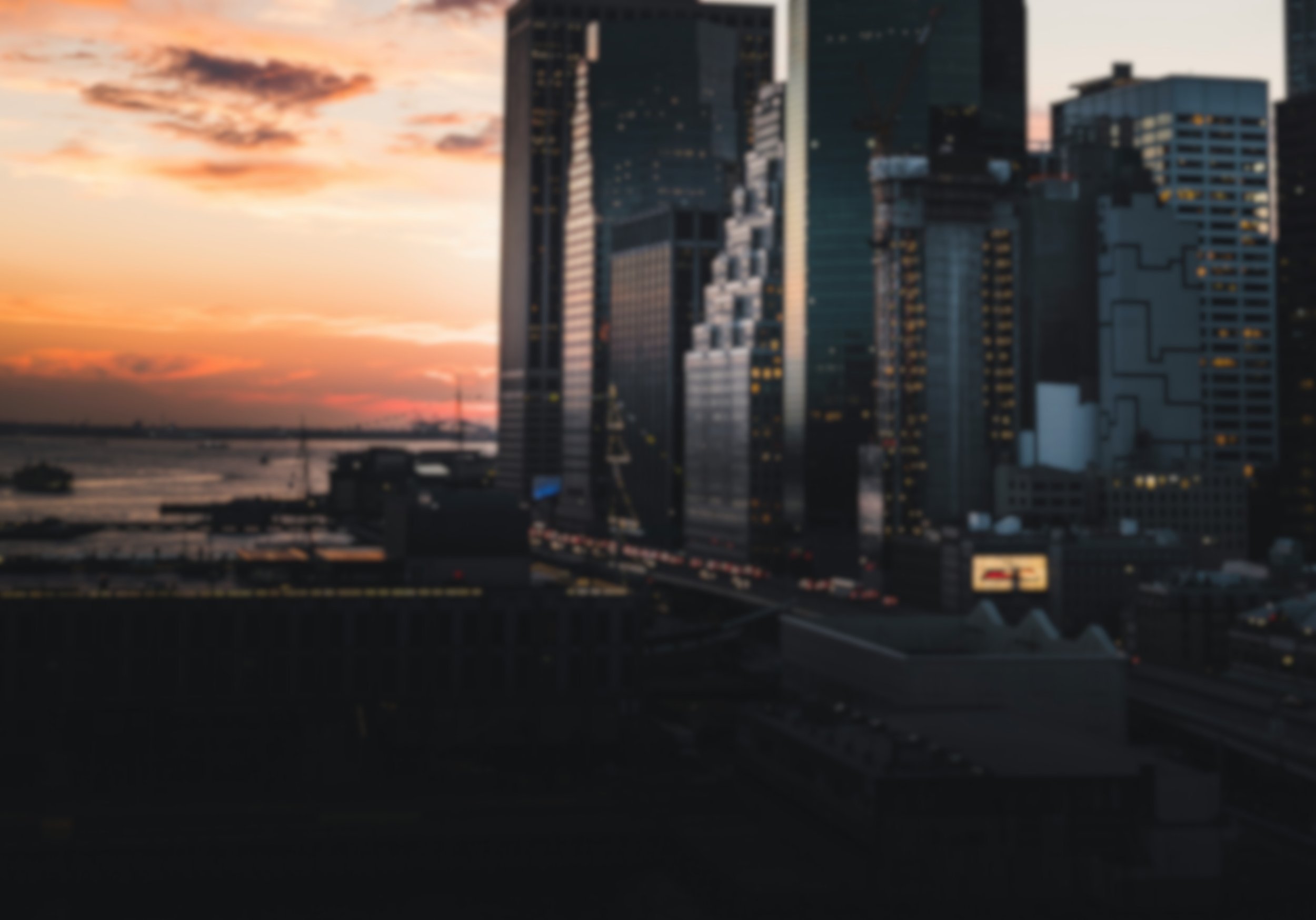 Blurry city skyline at sunset with tall buildings and water in the background