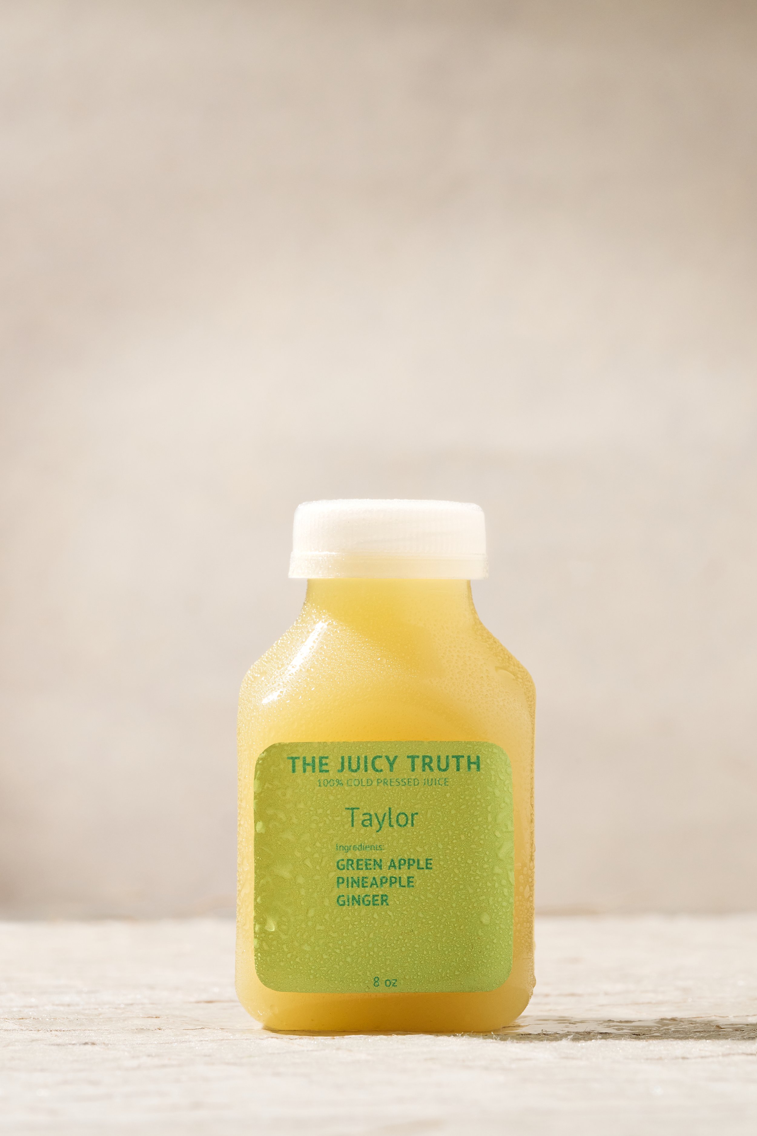 A bottle of cold pressed juice labeled 'The Juicy Truth' with ingredients green apple, pineapple, and ginger, placed on a light wooden surface.