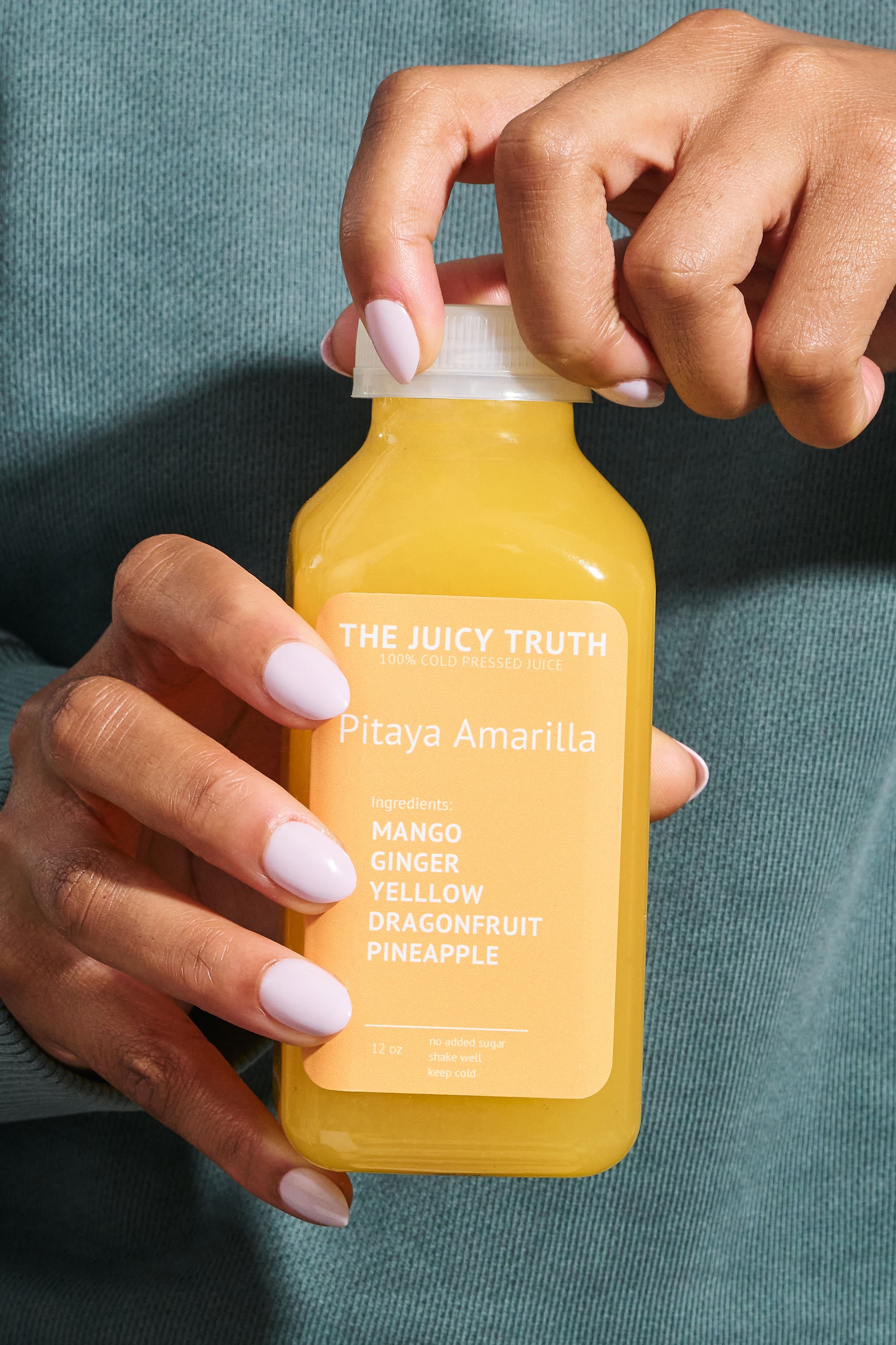 Person holding a bottle of yellow juice labeled 'Pitaya Amarilla' with ingredients listed as mango, ginger, yellow dragonfruit, and pineapple.