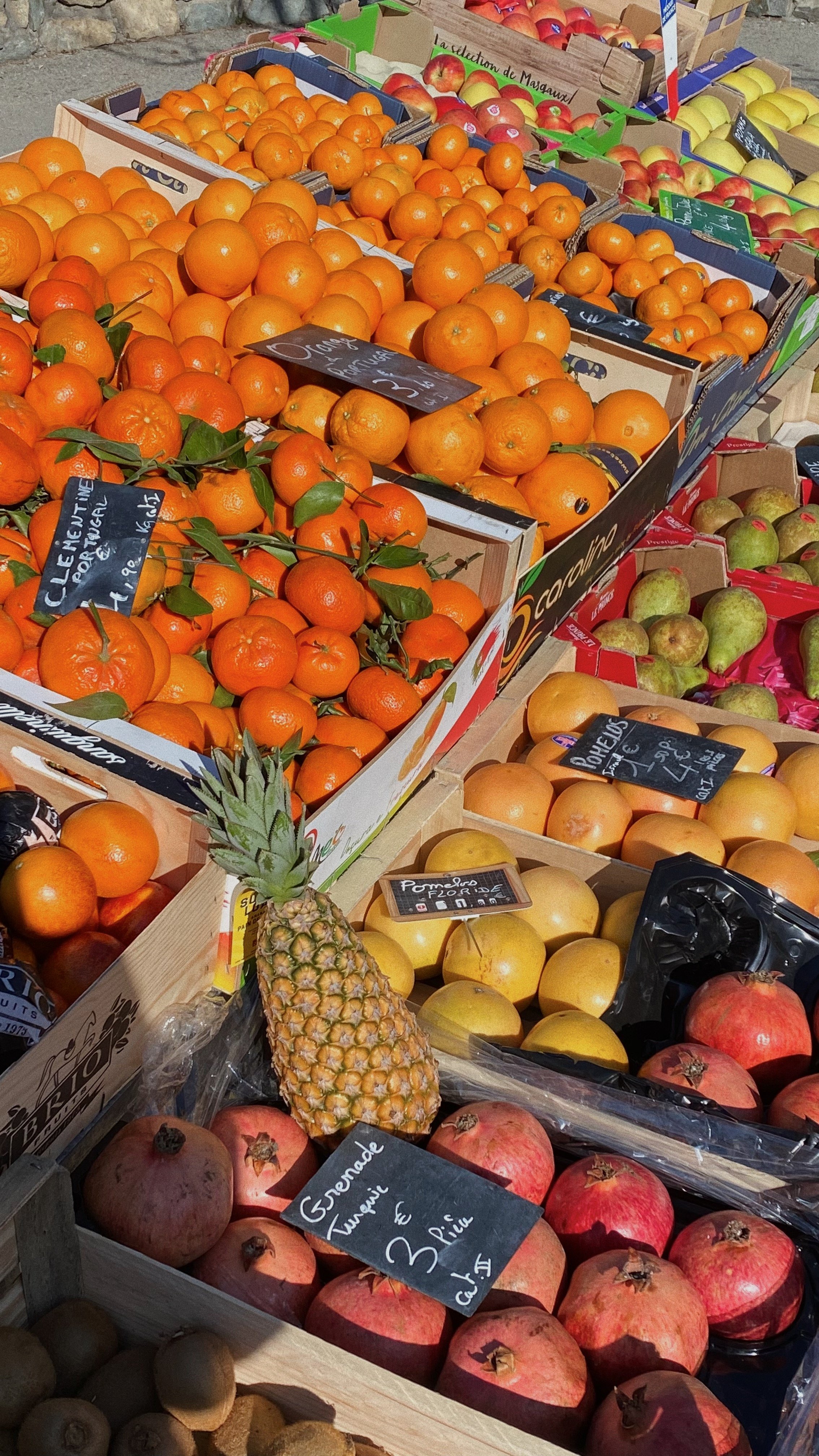A variety of fresh fruits displayed on a market stand, including oranges, apples, pineapples, pomegranates, and kiwis.