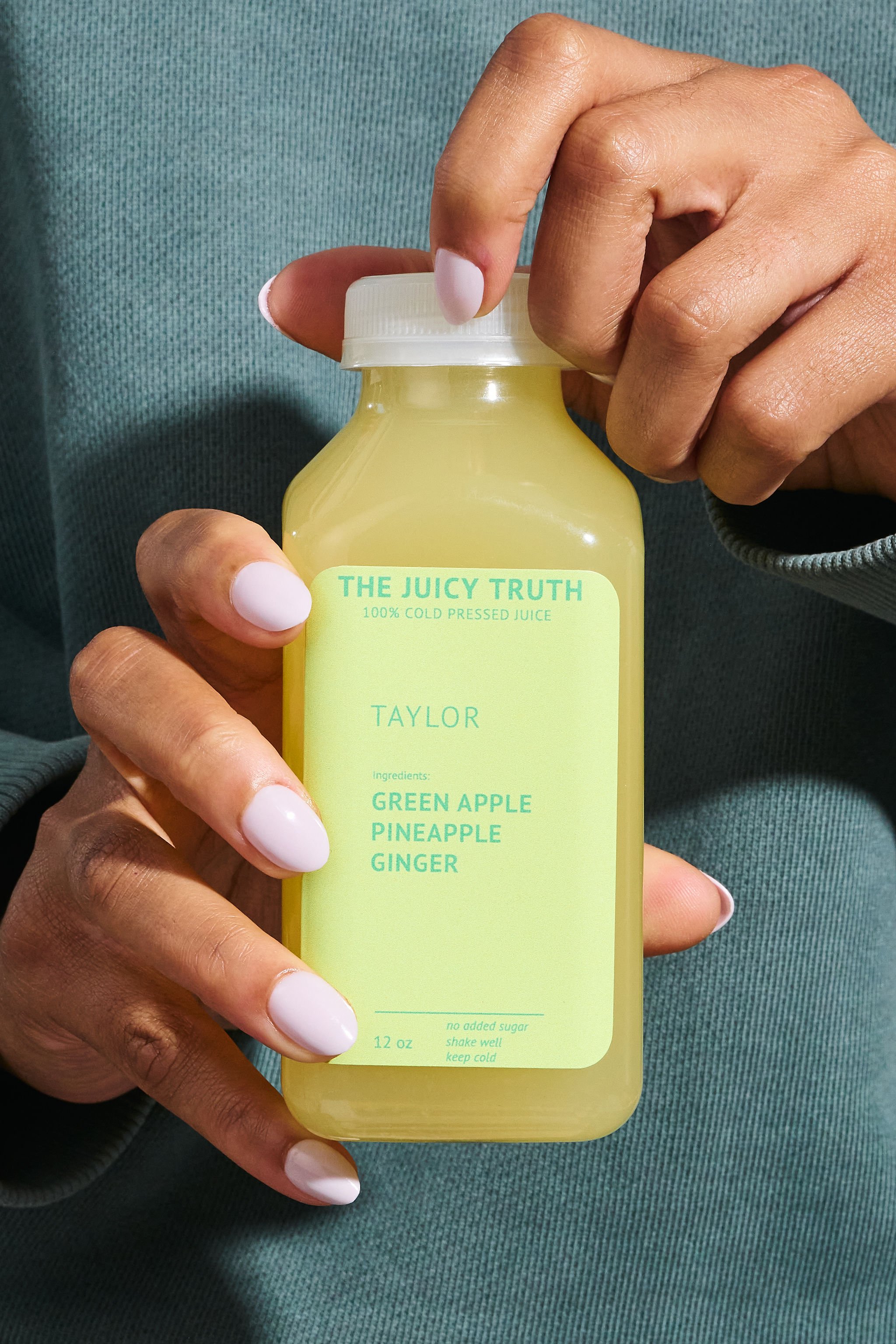 A person holding a yellow bottle labeled 'The Juicy Truth 100% Cold Pressed Juice' with ingredients listed as green apple, pineapple, and ginger