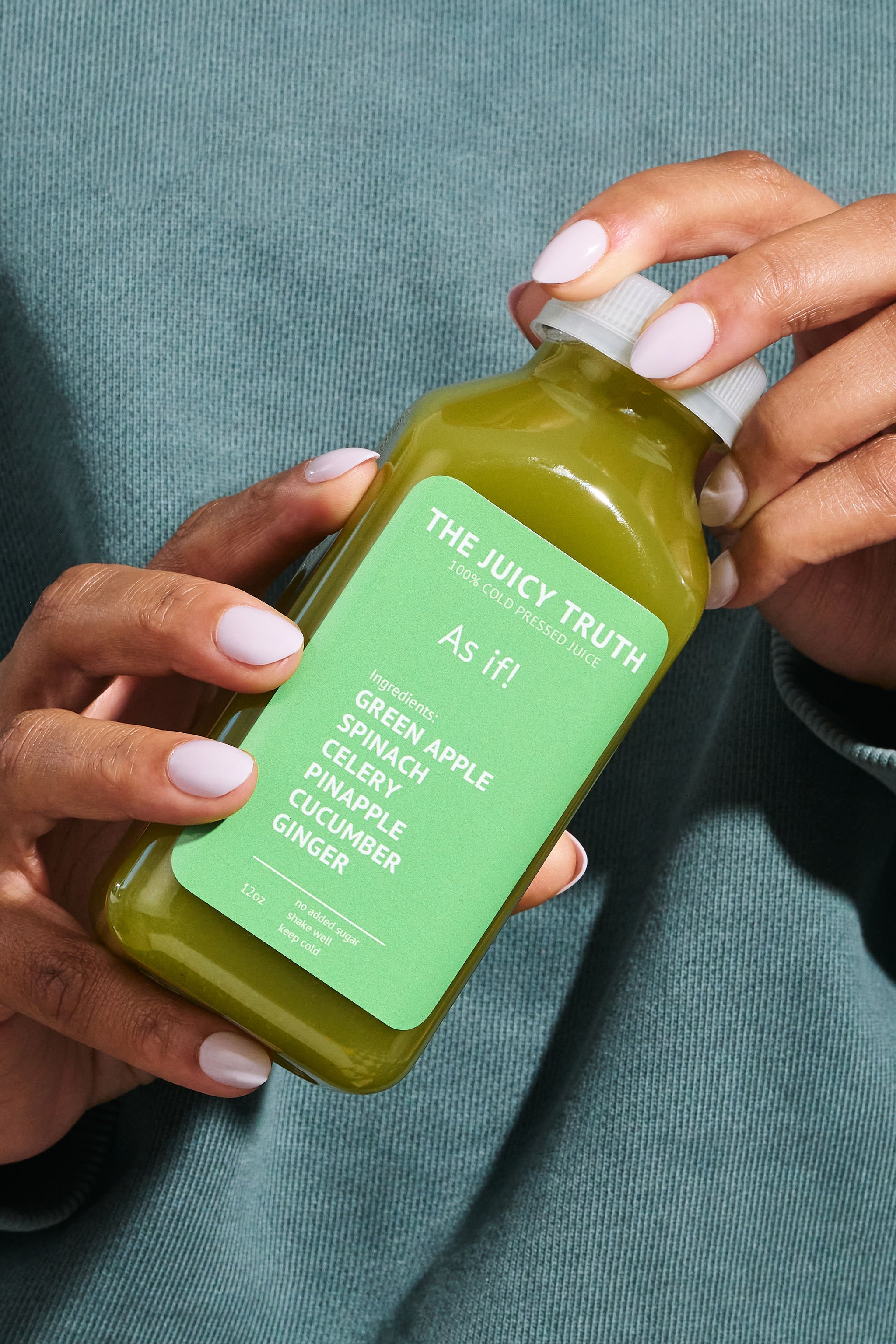 Person holding a green juice bottle labeled 'The Juicy Truth' with ingredients listed as green apple, spinach, celery, pineapple, cucumber, and ginger, against a teal background.