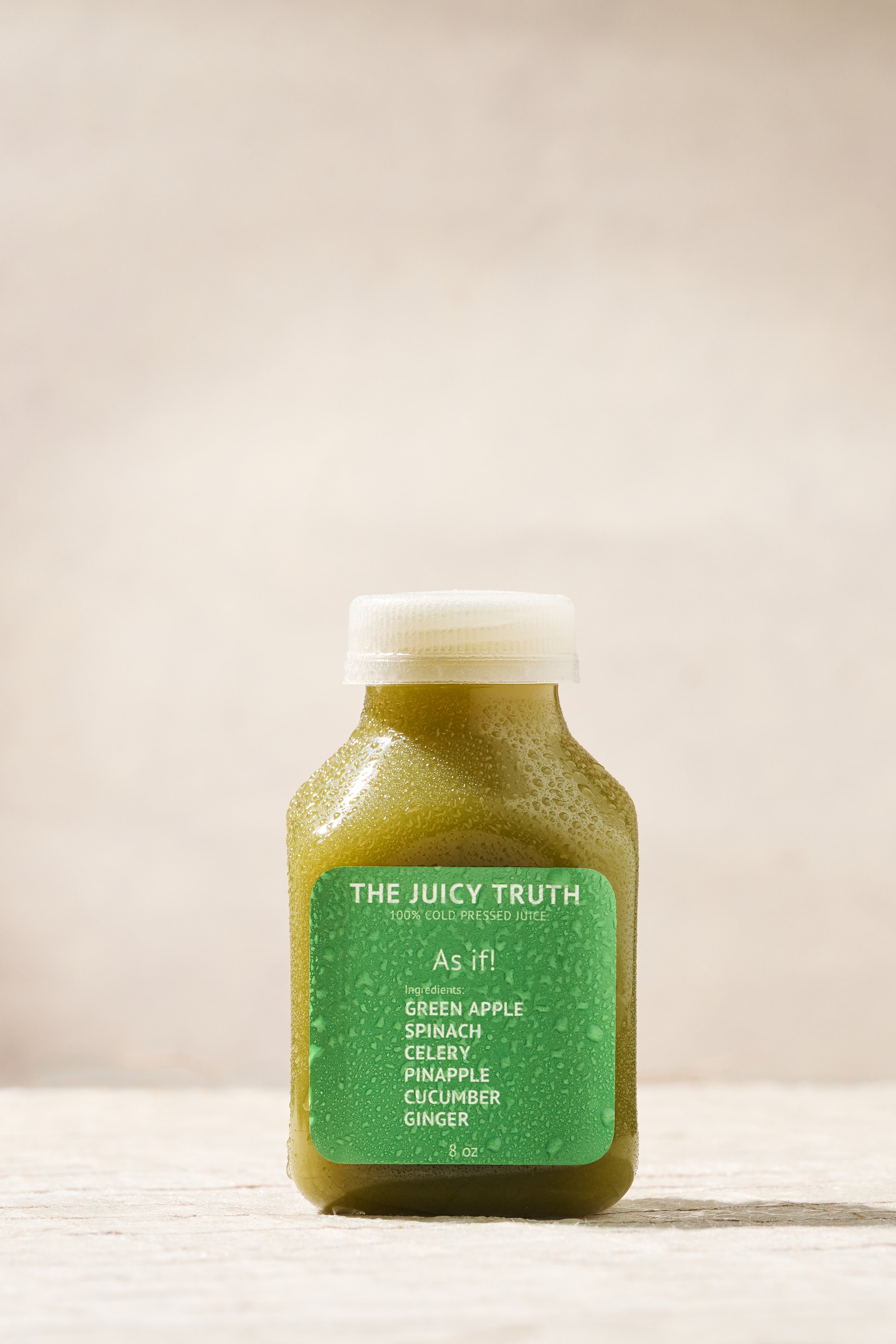 A small bottle of green juice with condensation on the outside, labeled 'The Juicy Truth' with ingredients including green apple, spinach, celery, pineapple, cucumber, and ginger.