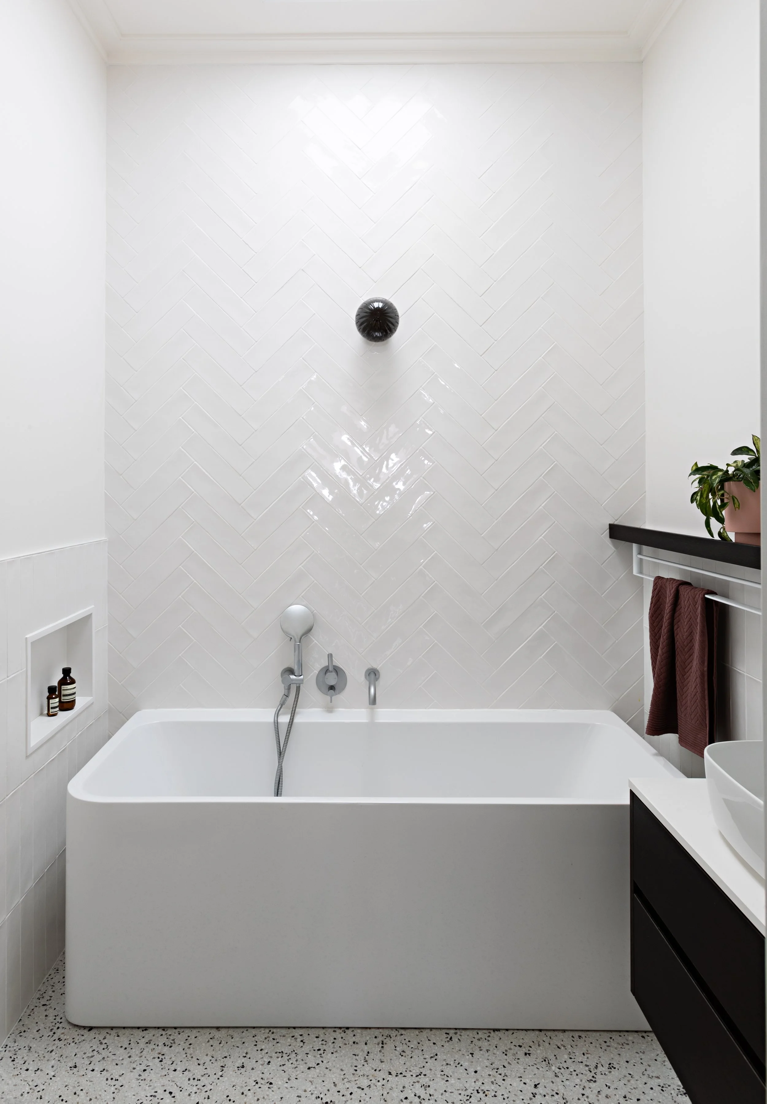 Brighton East House bathroom with freestanding bath and white herringbone tiled feature wall.