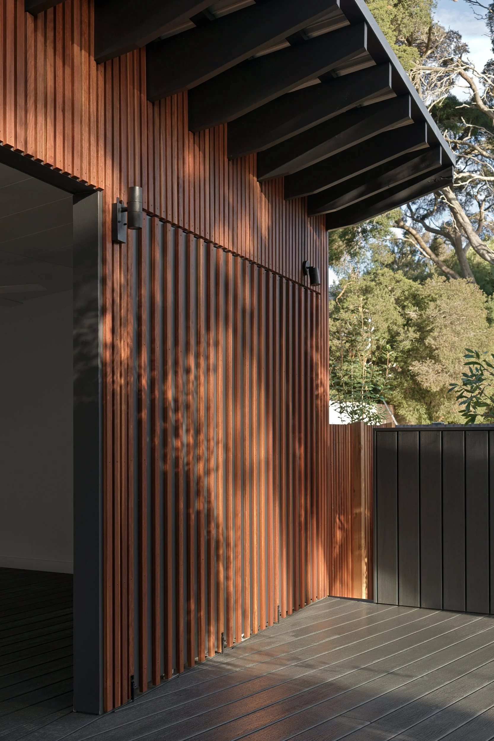 Timber-clad exterior of Cottesloe Retreat with a covered deck overlooking the surrounding trees.